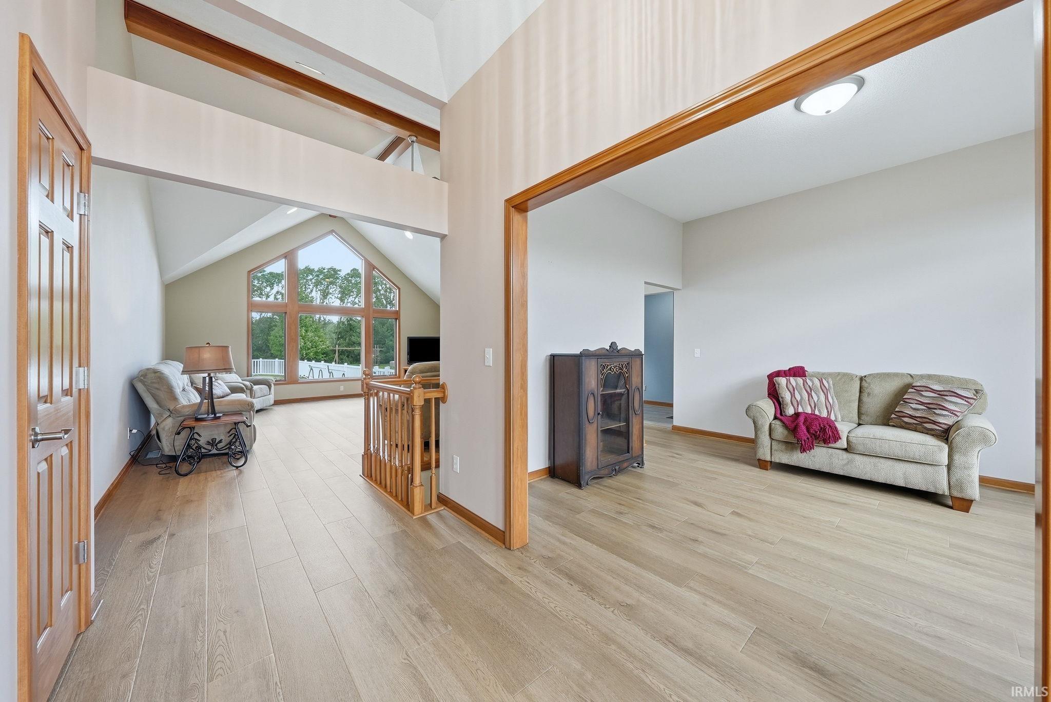 Open-concept living area featuring vaulted ceilings, wood-finish flooring, natural wood door frames, and a prominent picture window