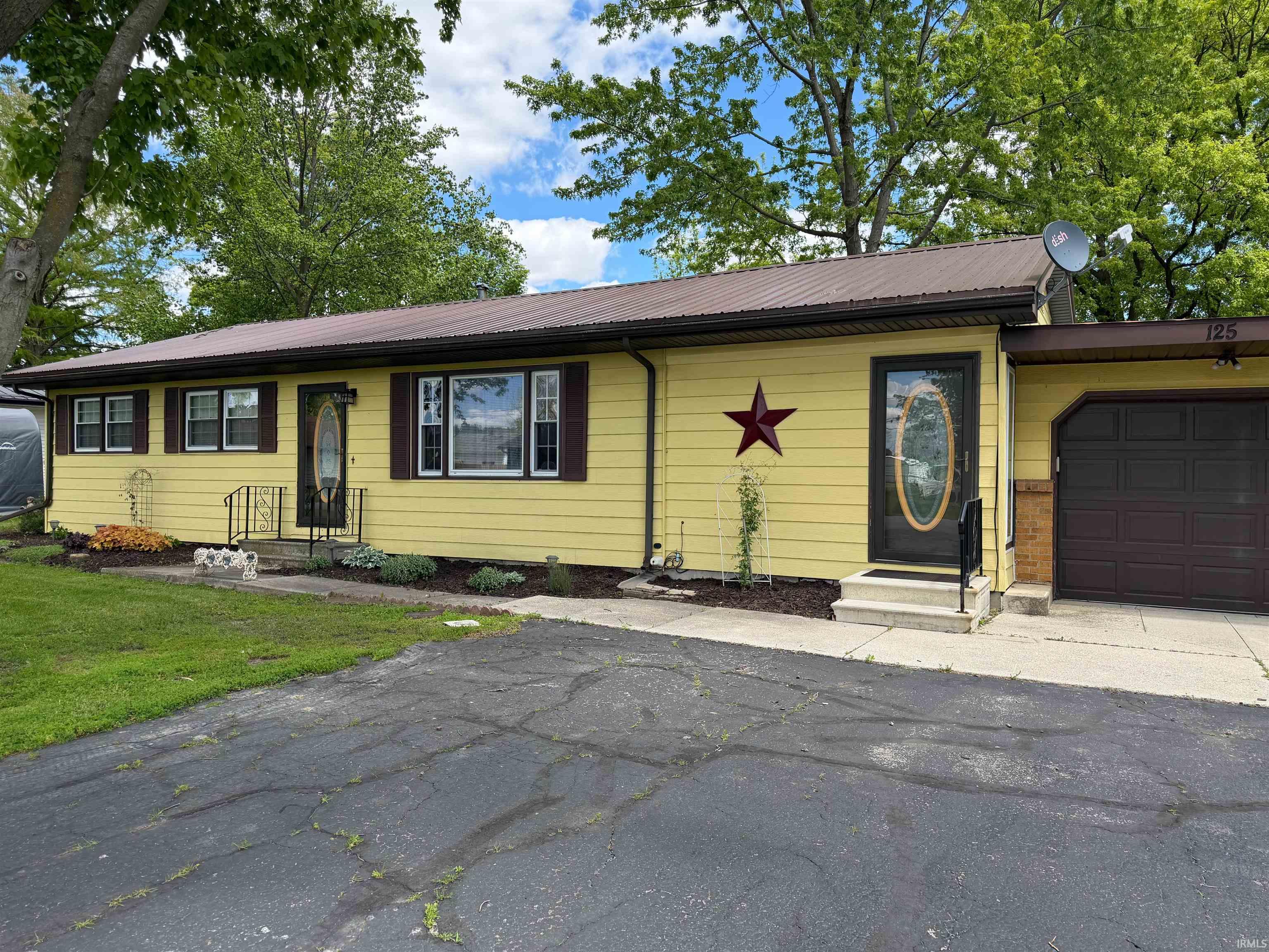 Ranch-style residence featuring a yellow siding exterior, brown metal roof, and an attached garage with a dark brown door