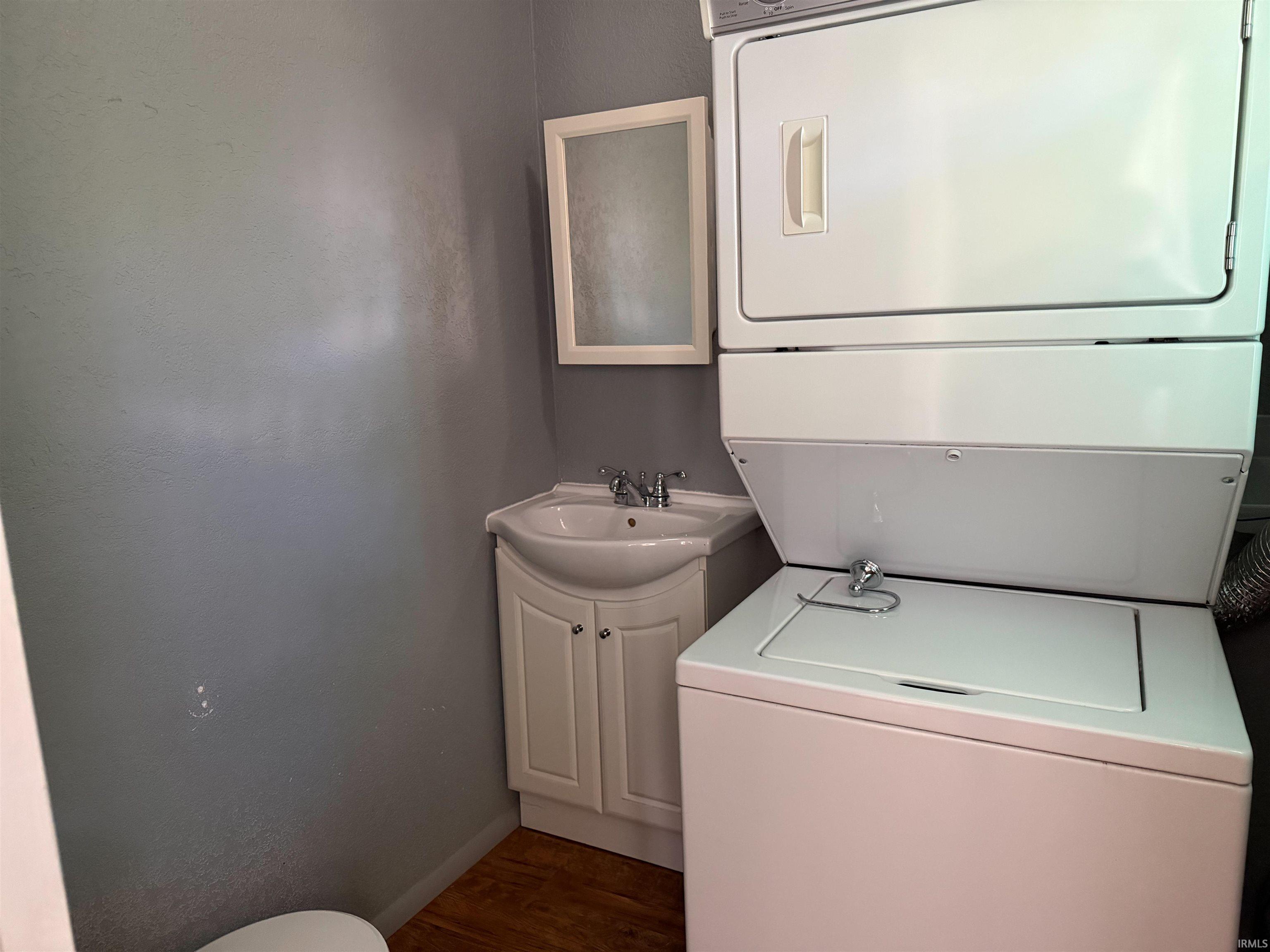 Dedicated laundry area featuring a white stackable washer and dryer, a white pedestal sink with a matching vanity cabinet, a recessed medicine cabinet, and wood-finish flooring