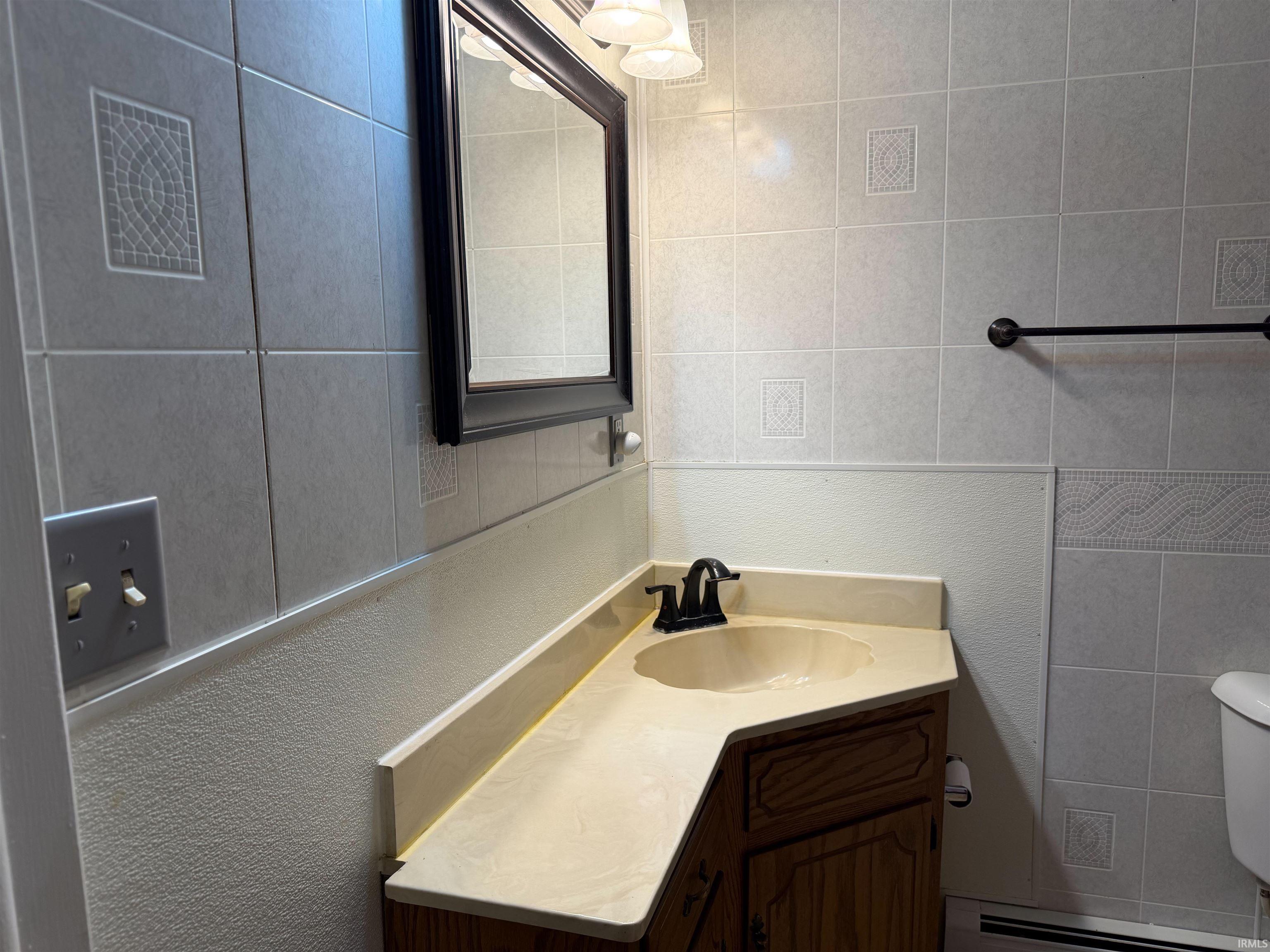 Bathroom vanity featuring a light-toned countertop with integrated sink, wood-finish cabinetry, and a dark-framed mirror
