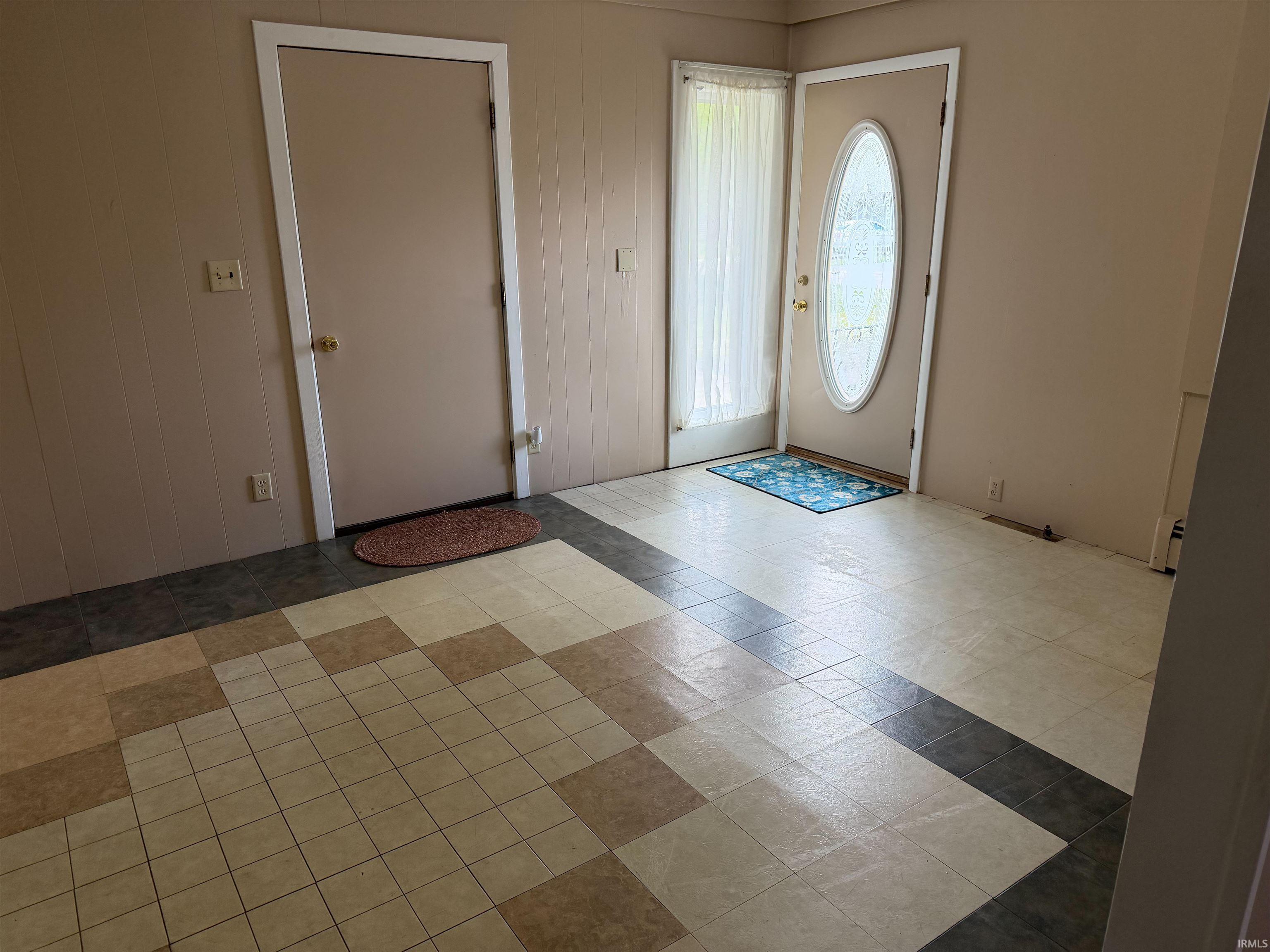 Entryway featuring patterned tile flooring, light-colored walls, a solid panel interior door, and an exterior door with an oval-shaped frosted glass insert