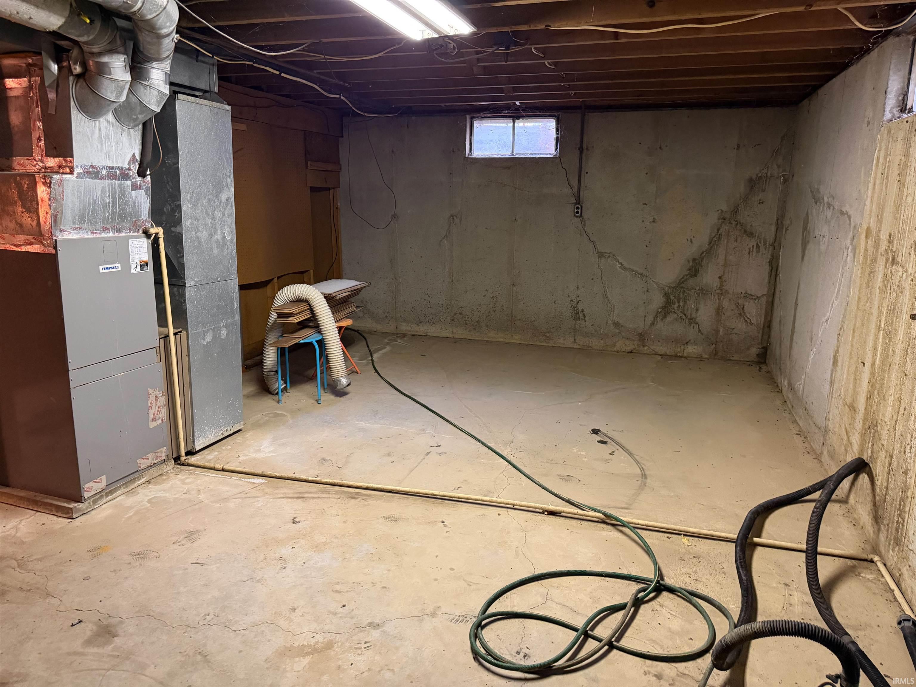 Unfinished basement featuring exposed joists, concrete flooring, and a single window