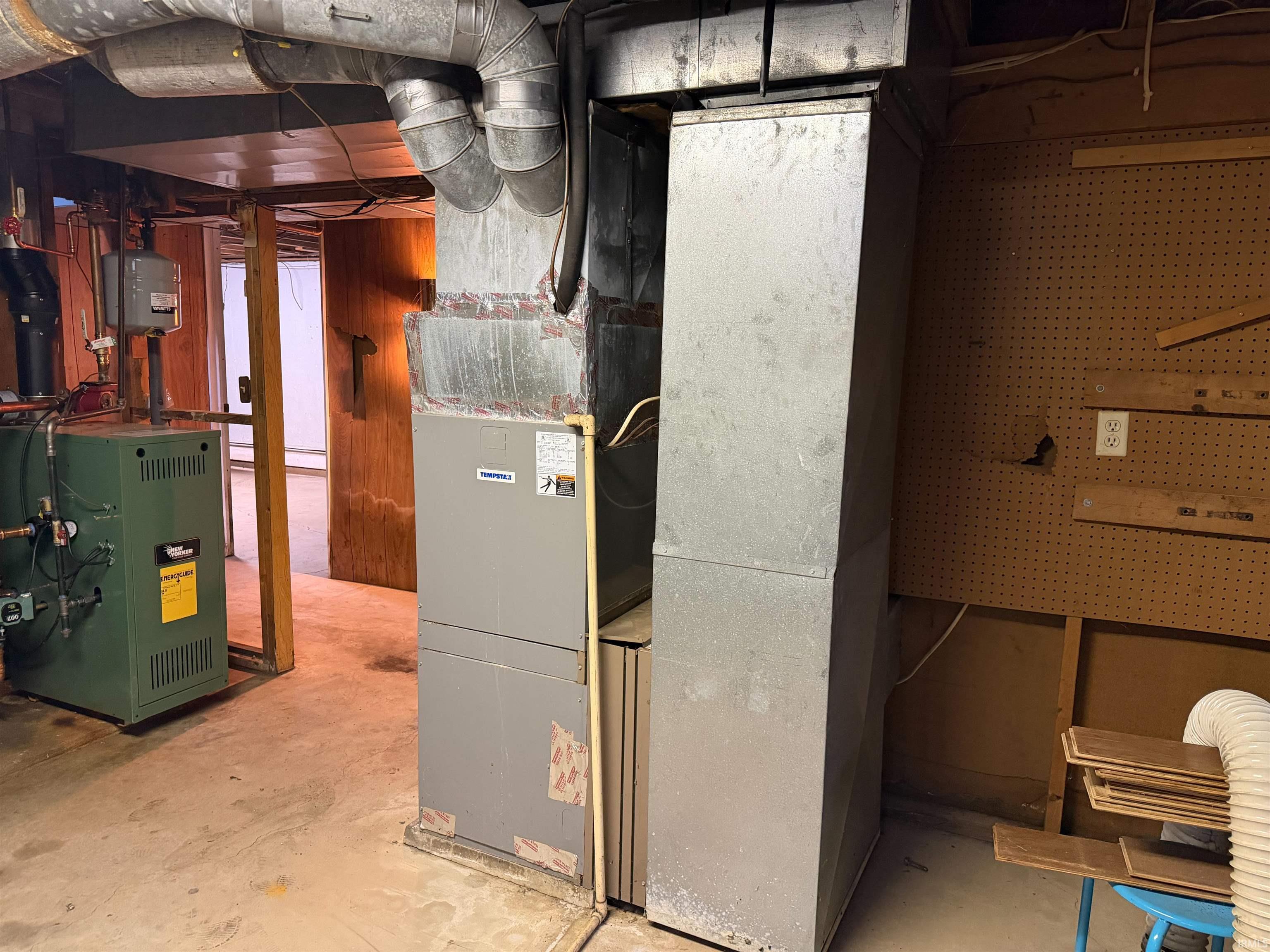 Basement utility area featuring a forced-air furnace unit, a green boiler system, exposed metal ductwork, and a pegboard wall
