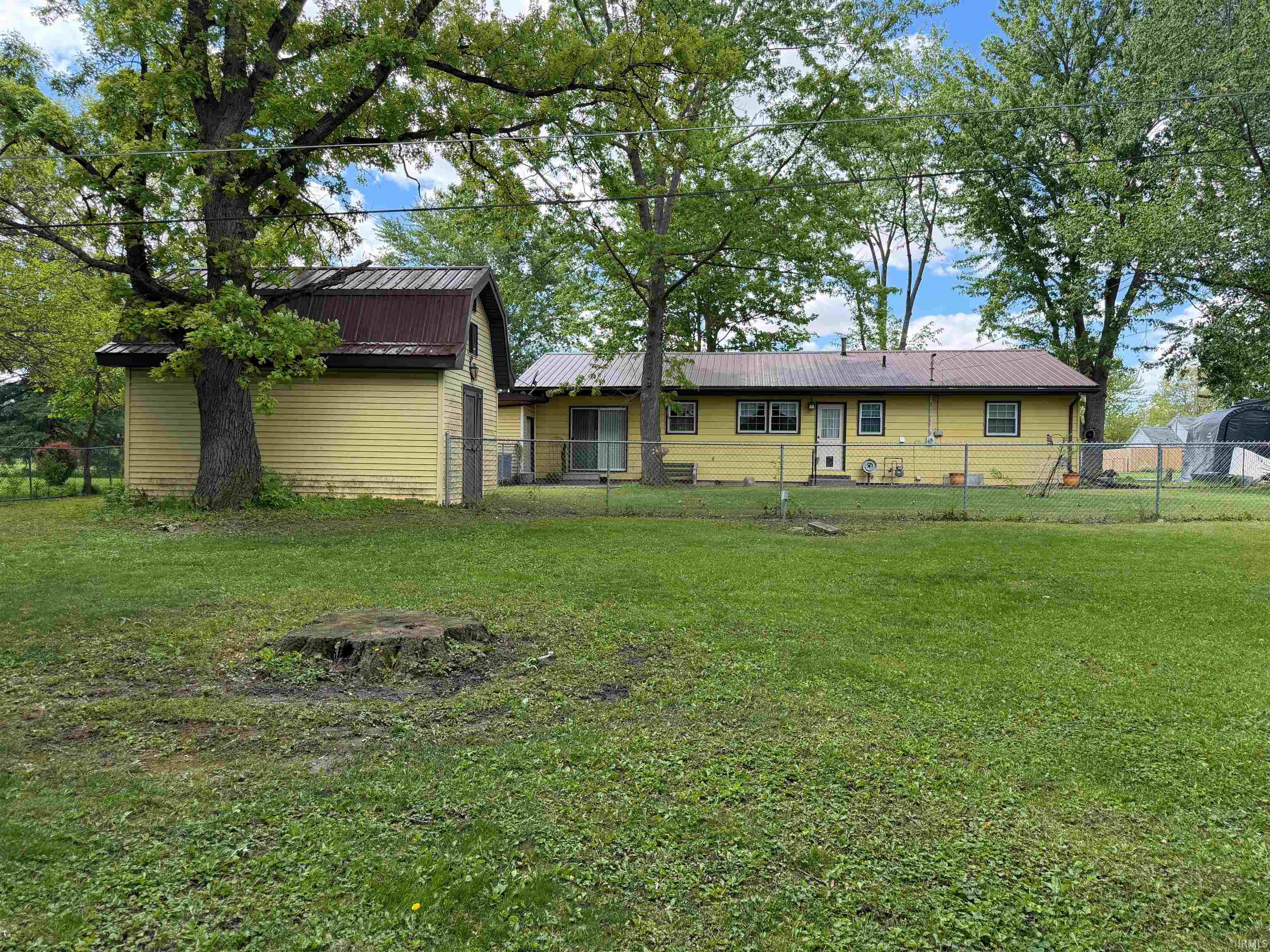 Expansive backyard featuring a chain-link fence, mature trees, and a detached outbuilding with a metal roof