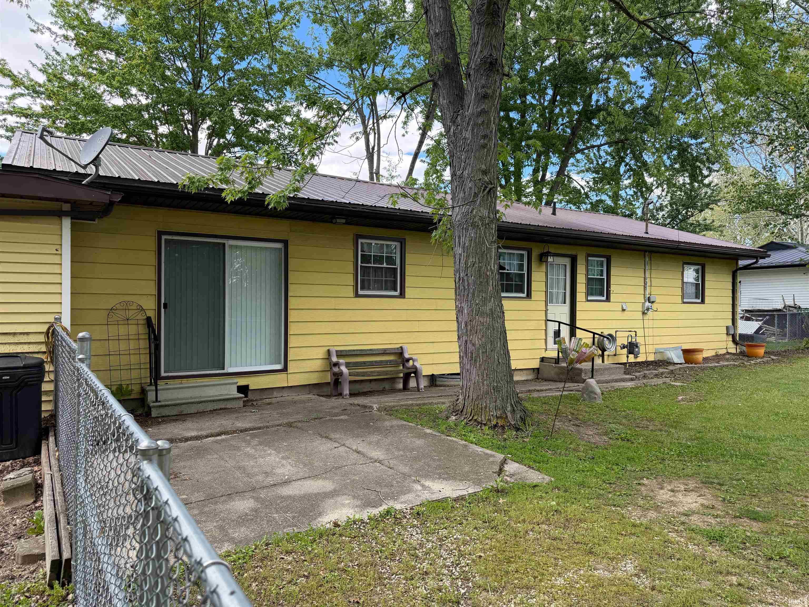 Exterior featuring yellow siding, a metal roof, and a concrete patio