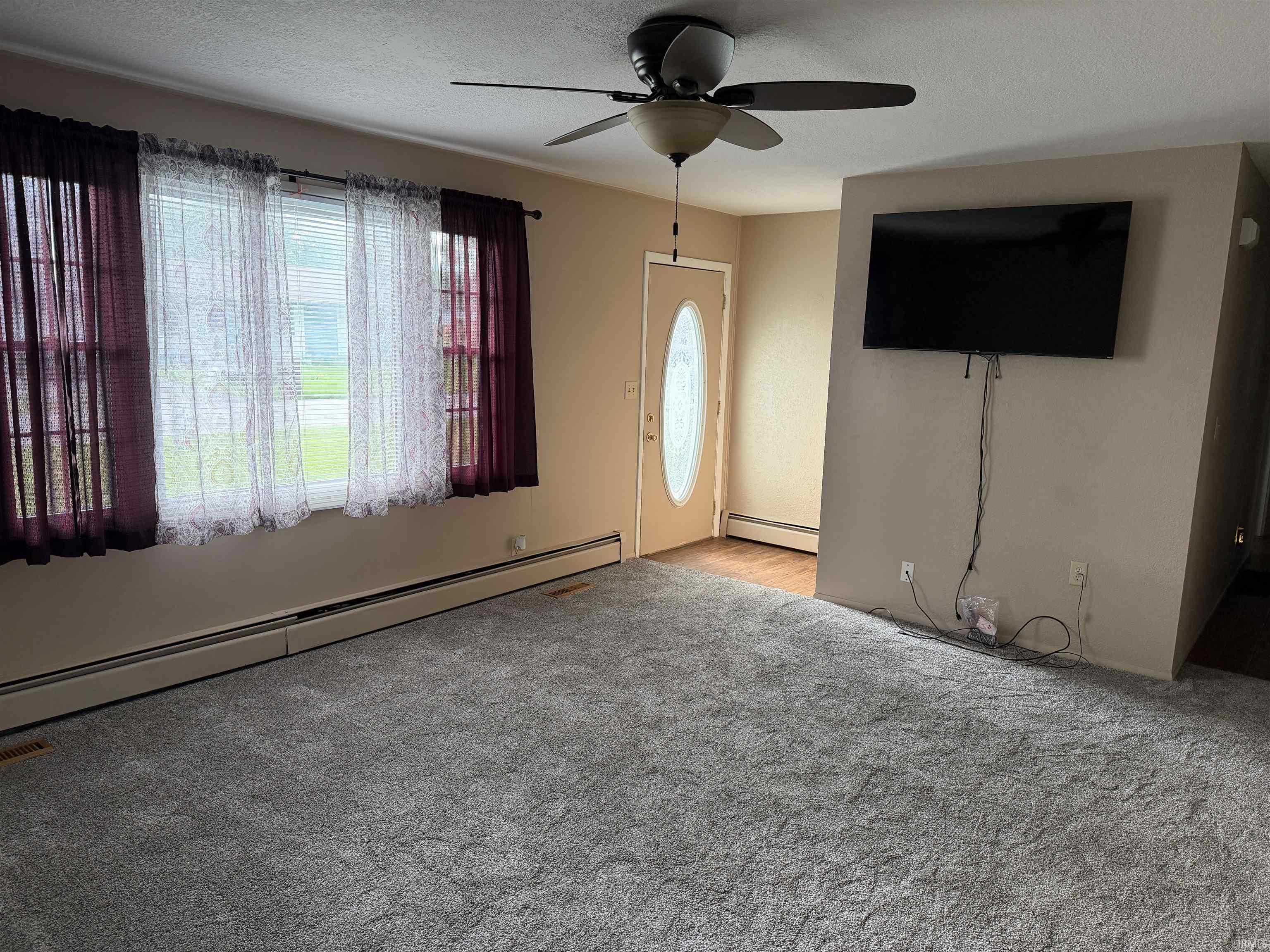 Living area featuring light gray carpeting, neutral wall tones, and a front entry door with an oval glass insert