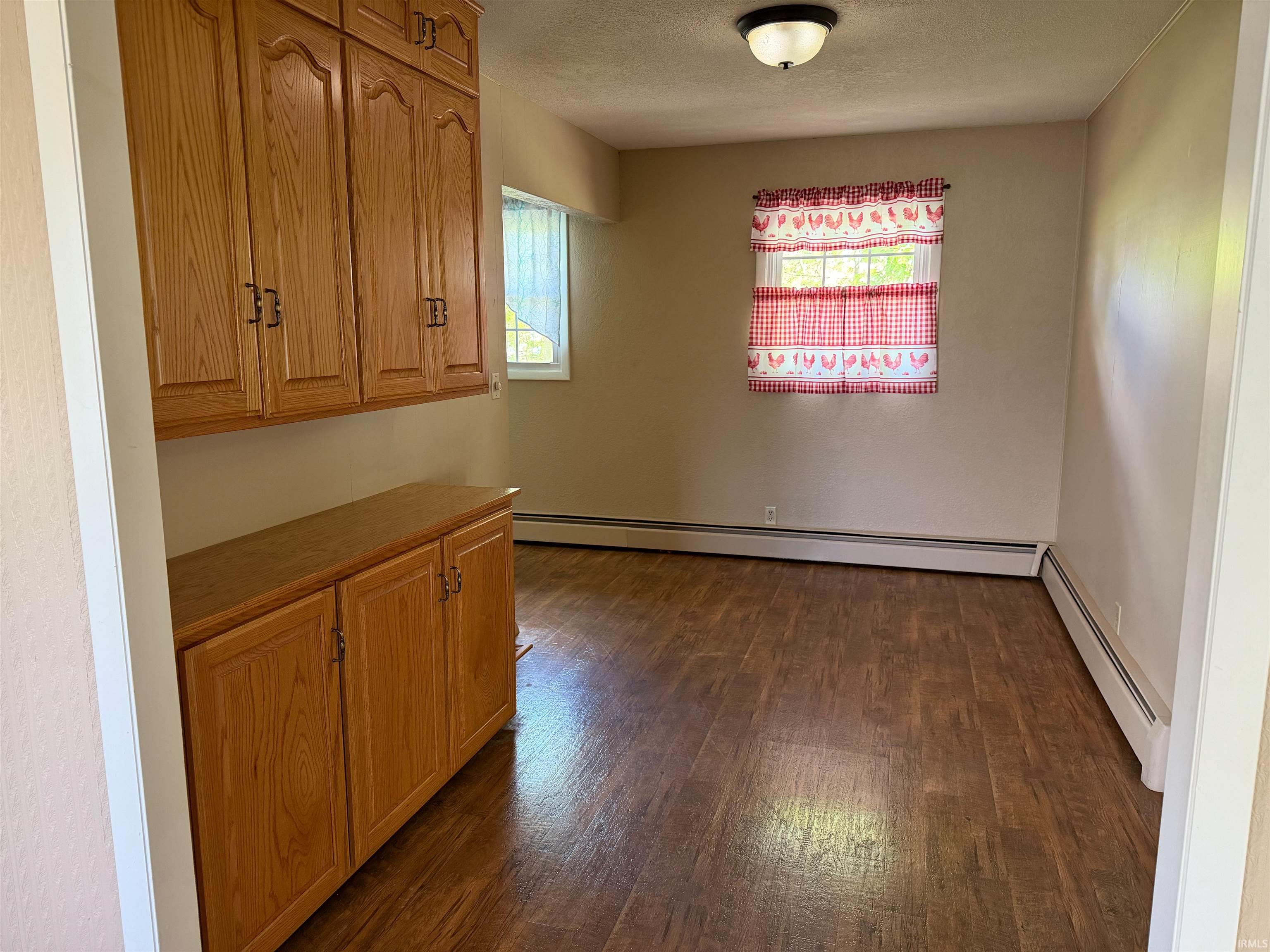 Built-in wood cabinetry with upper and lower storage, wood-finish flooring, and baseboard heating