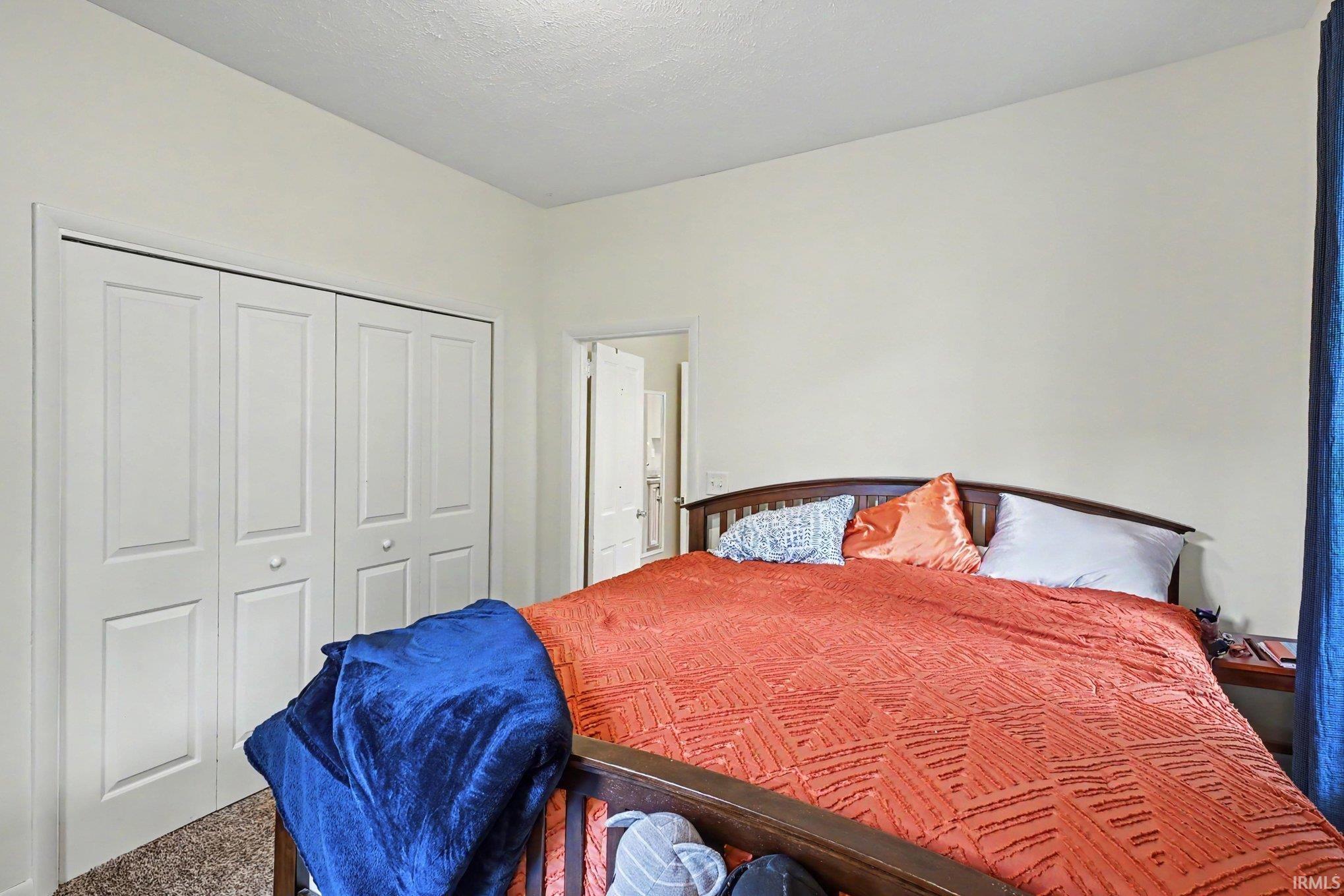Bedroom featuring neutral wall paint, bi-fold closet doors with panel detailing, and textured carpet flooring