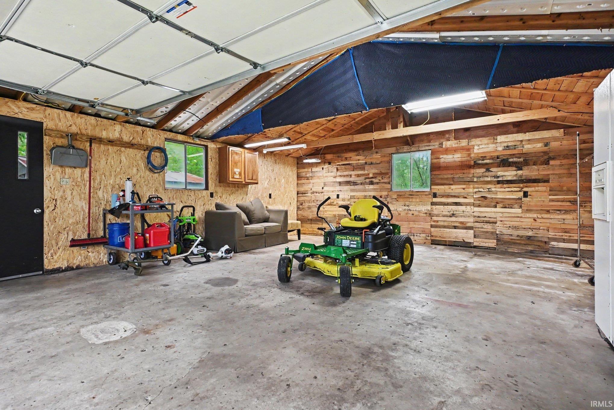 Spacious garage with high ceilings, exposed wood beams, concrete flooring, and multiple windows providing natural light