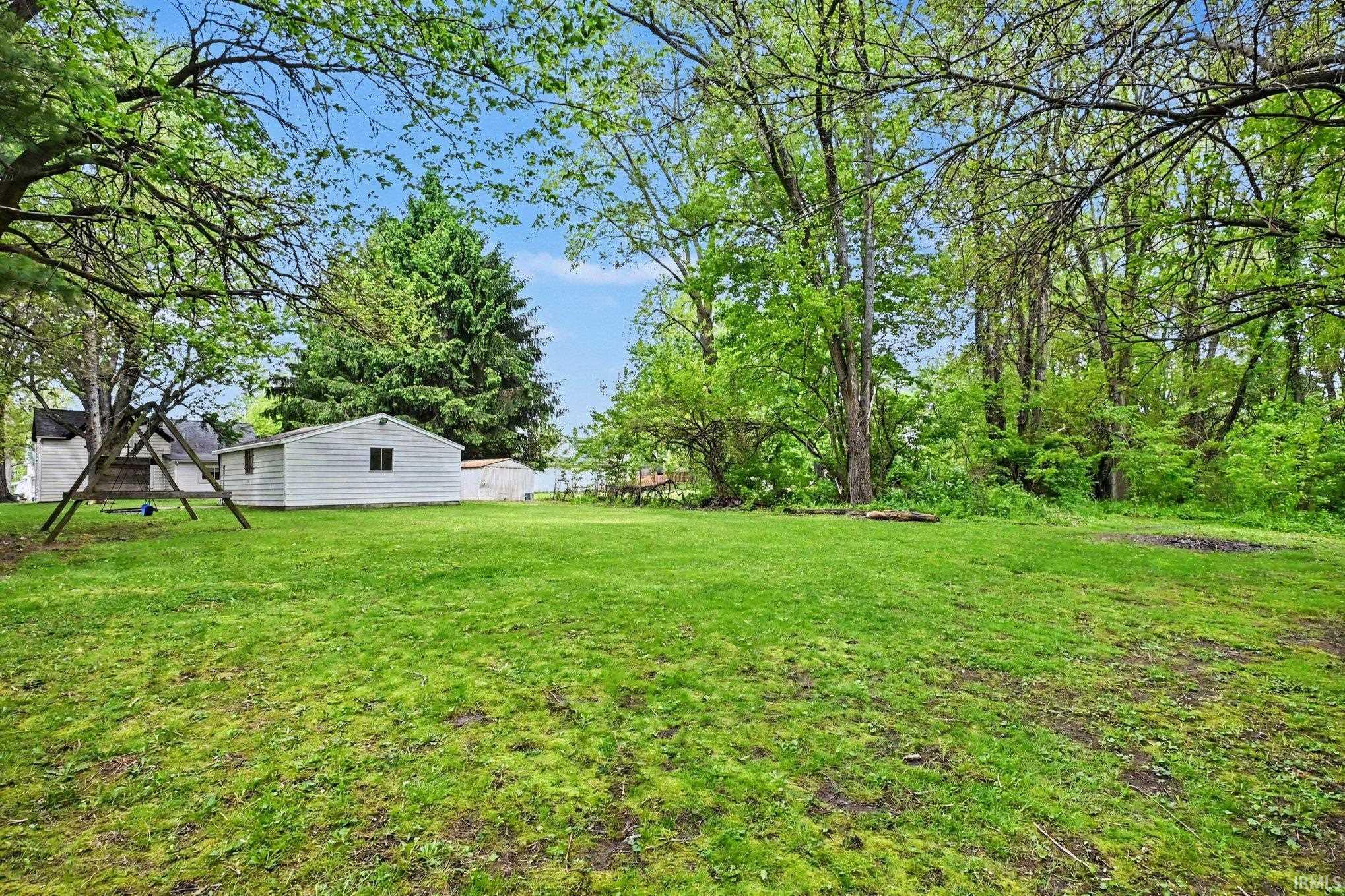 Expansive green lawn surrounded by mature trees, featuring a white detached outbuilding with a window