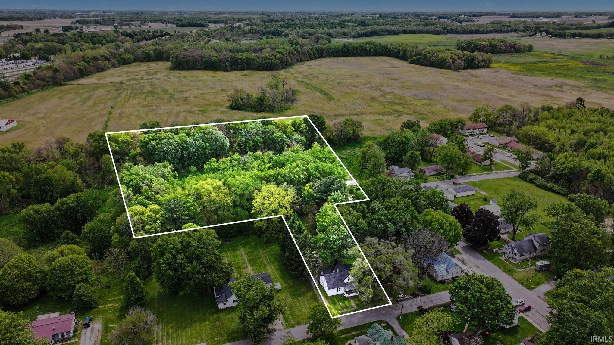Aerial perspective highlighting a property with a significant wooded area and a residential structure