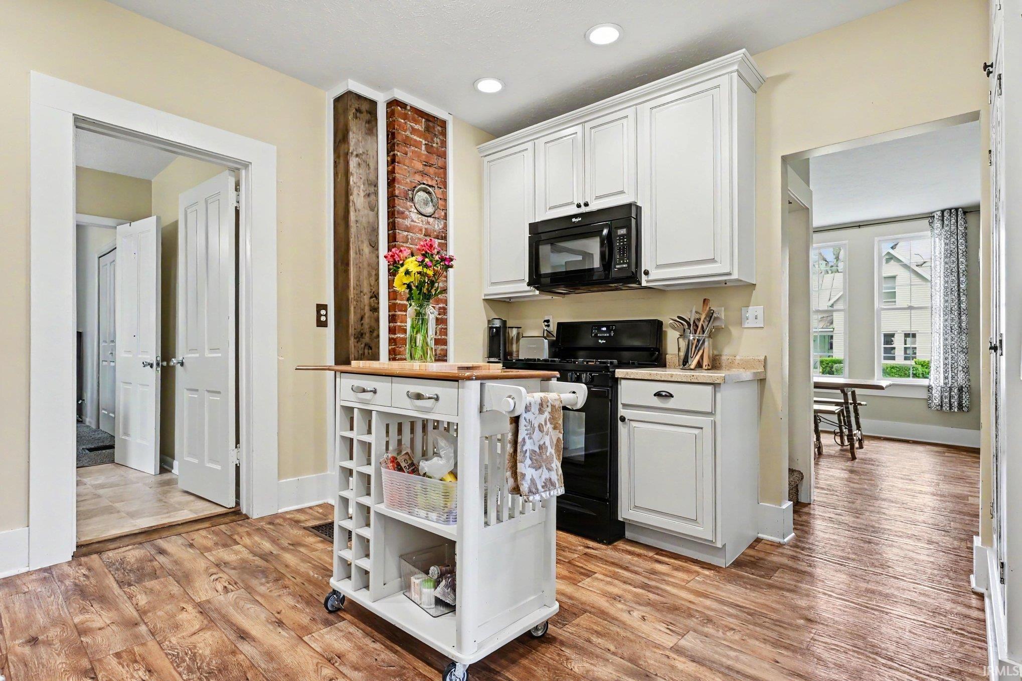 Kitchen featuring wood-finish flooring, white cabinetry, black appliances, and a visible brick column