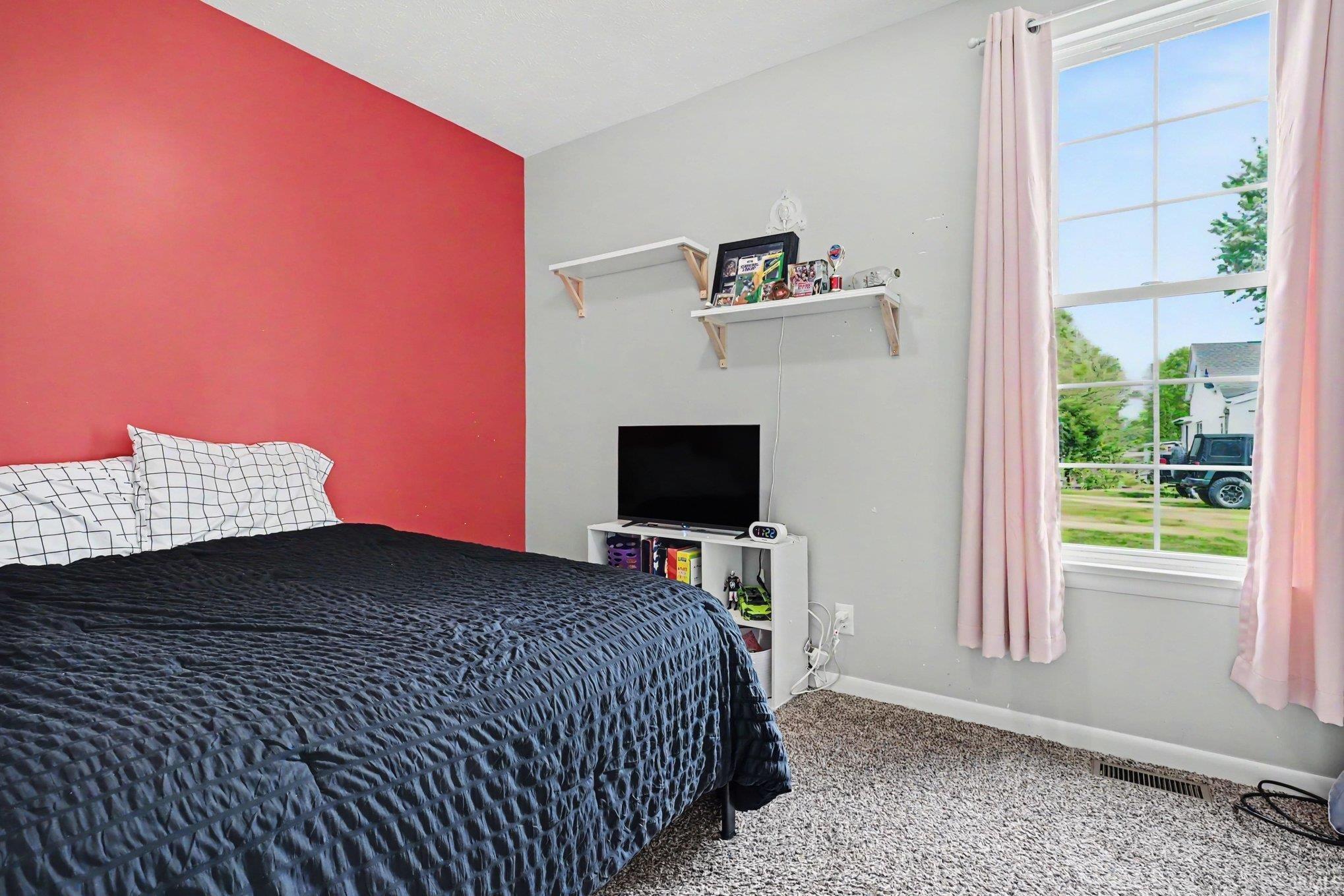 Carpeted room featuring a single large window with white framing, a red accent wall, and light gray painted walls