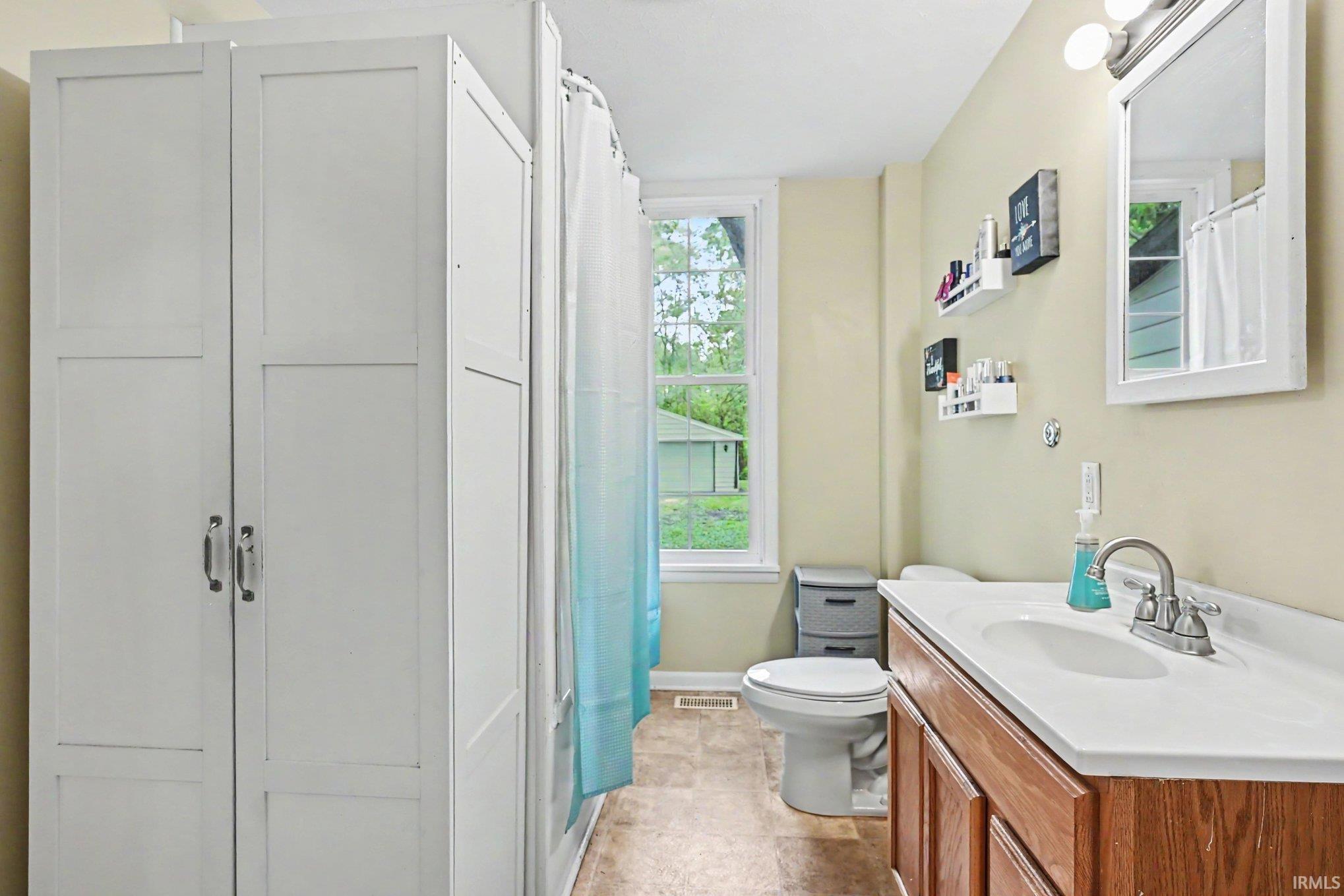 Bathroom featuring a wood-finish vanity with a white countertop and integrated sink, a wall-mounted mirror, and a window with natural light