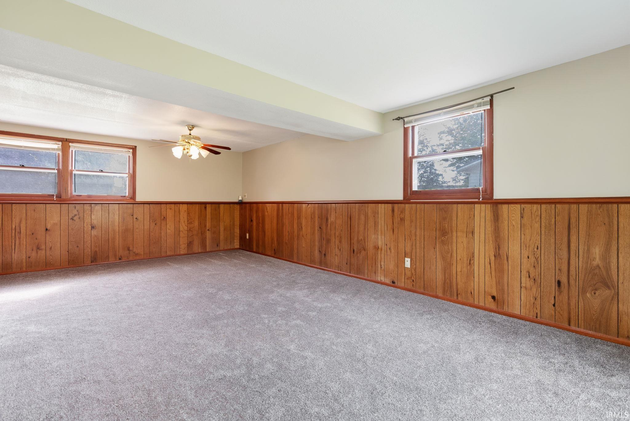 Spacious room featuring wood paneling, light gray carpeting, and multiple windows