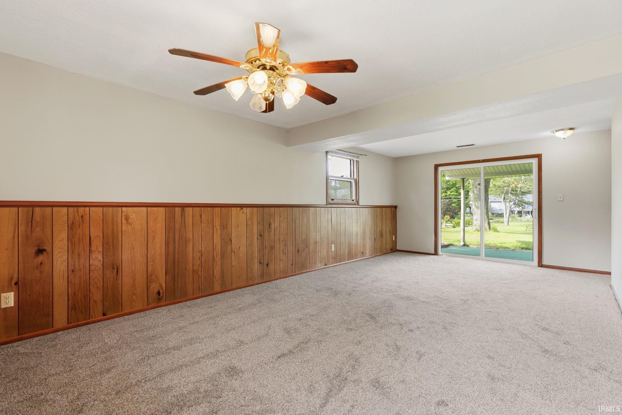Spacious room featuring light-colored carpeting and wood paneling along the lower walls