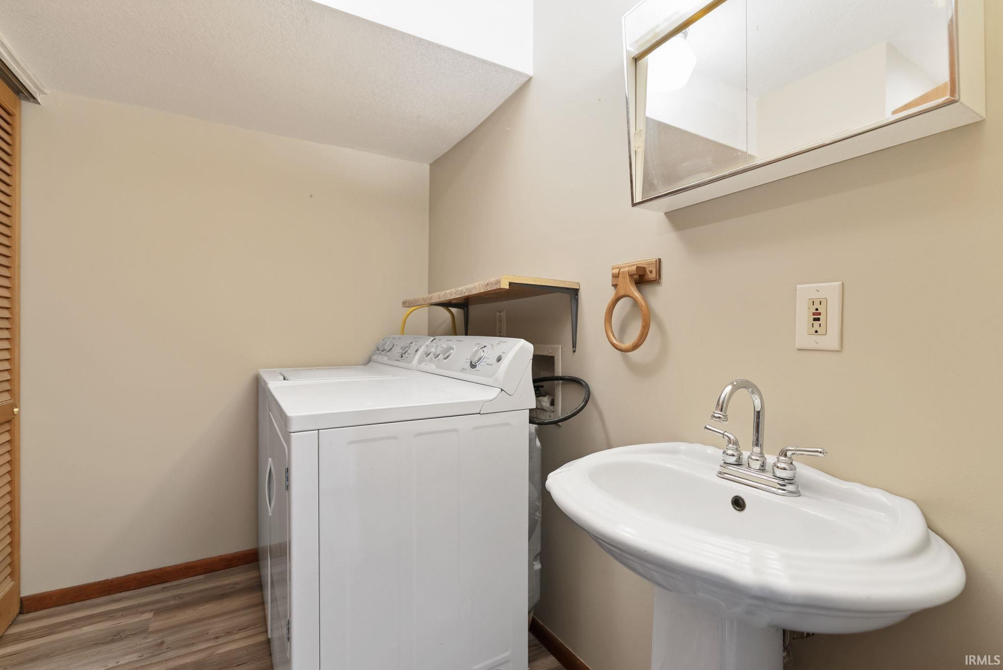 Utility area featuring a pedestal sink with chrome faucet, wood-finish flooring, a built-in shelf, and a louvered door