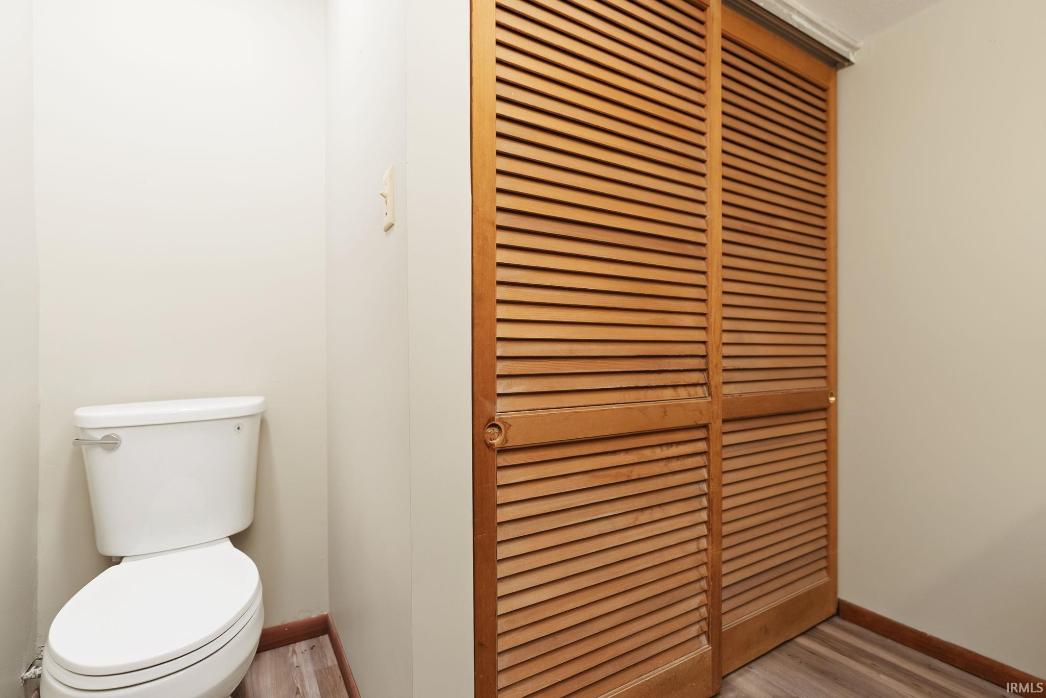 Louvered bi-fold closet doors paired with a compact white toilet and wood-finish flooring