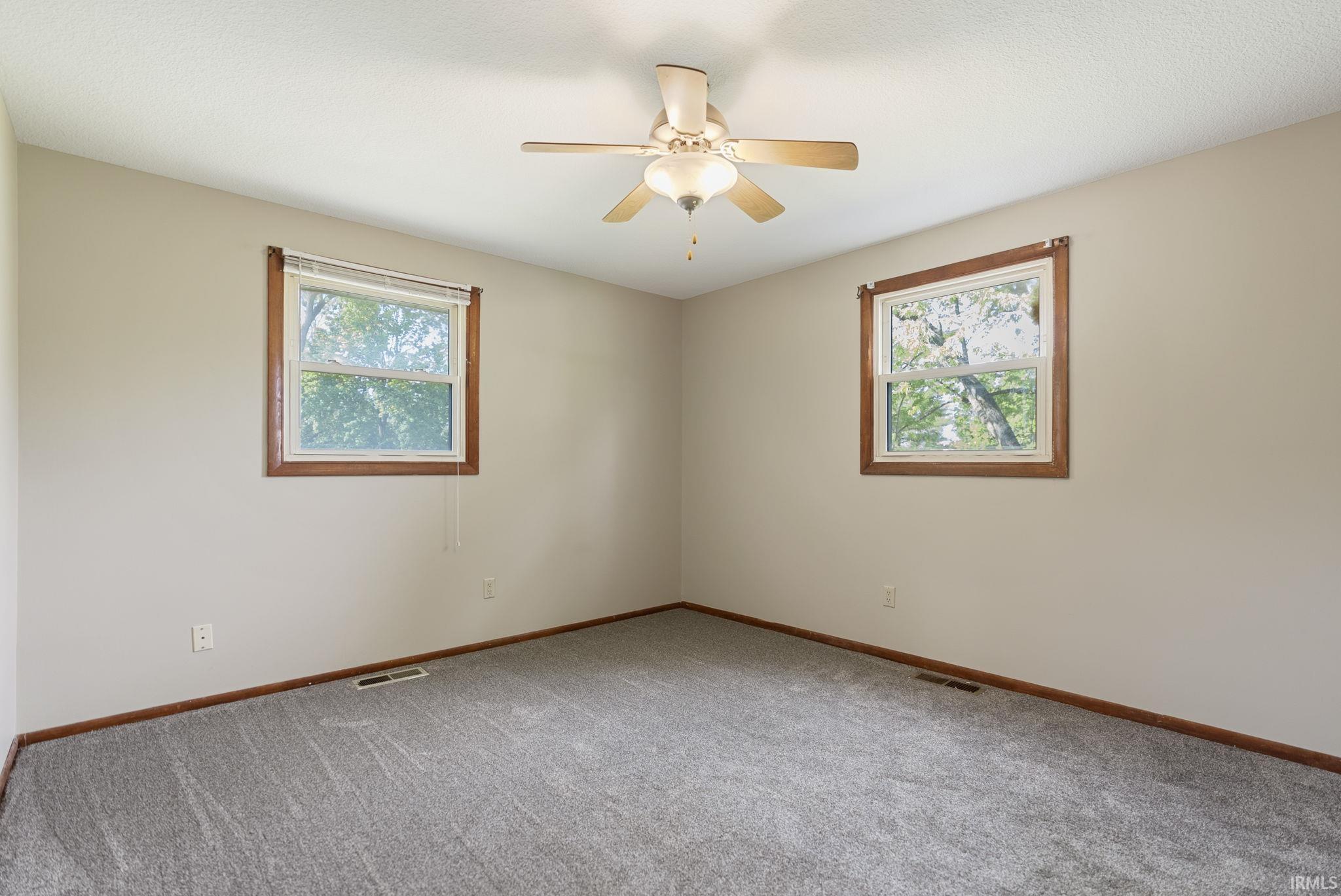Neutral wall tones with wood trim windows featuring a ceiling fan, textured ceiling, and gray carpeting