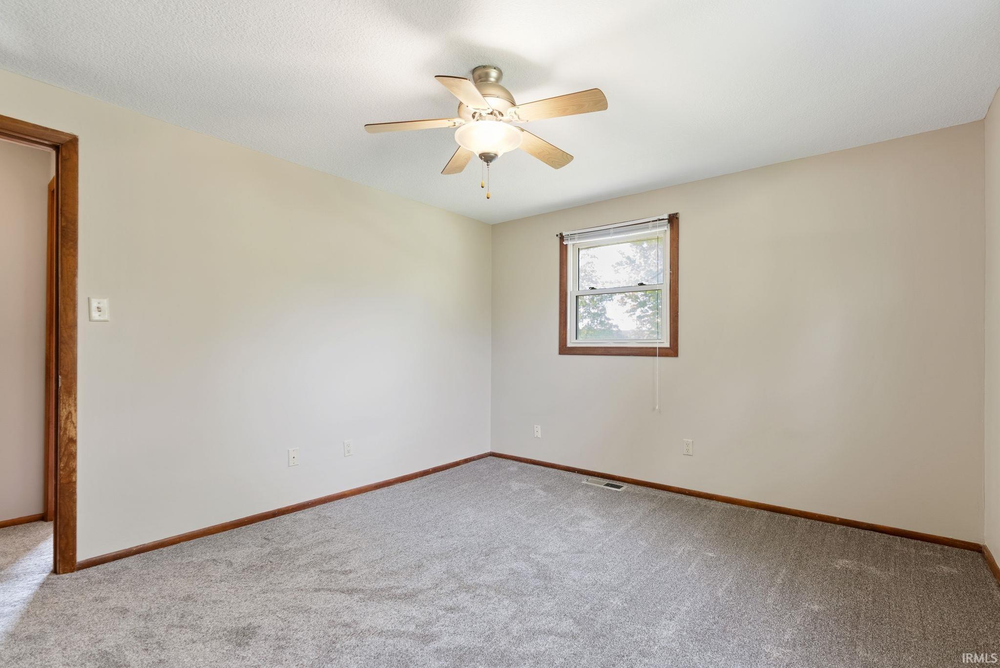 Carpeted room featuring a ceiling fan with light fixture, a window with wood trim, and wood baseboards