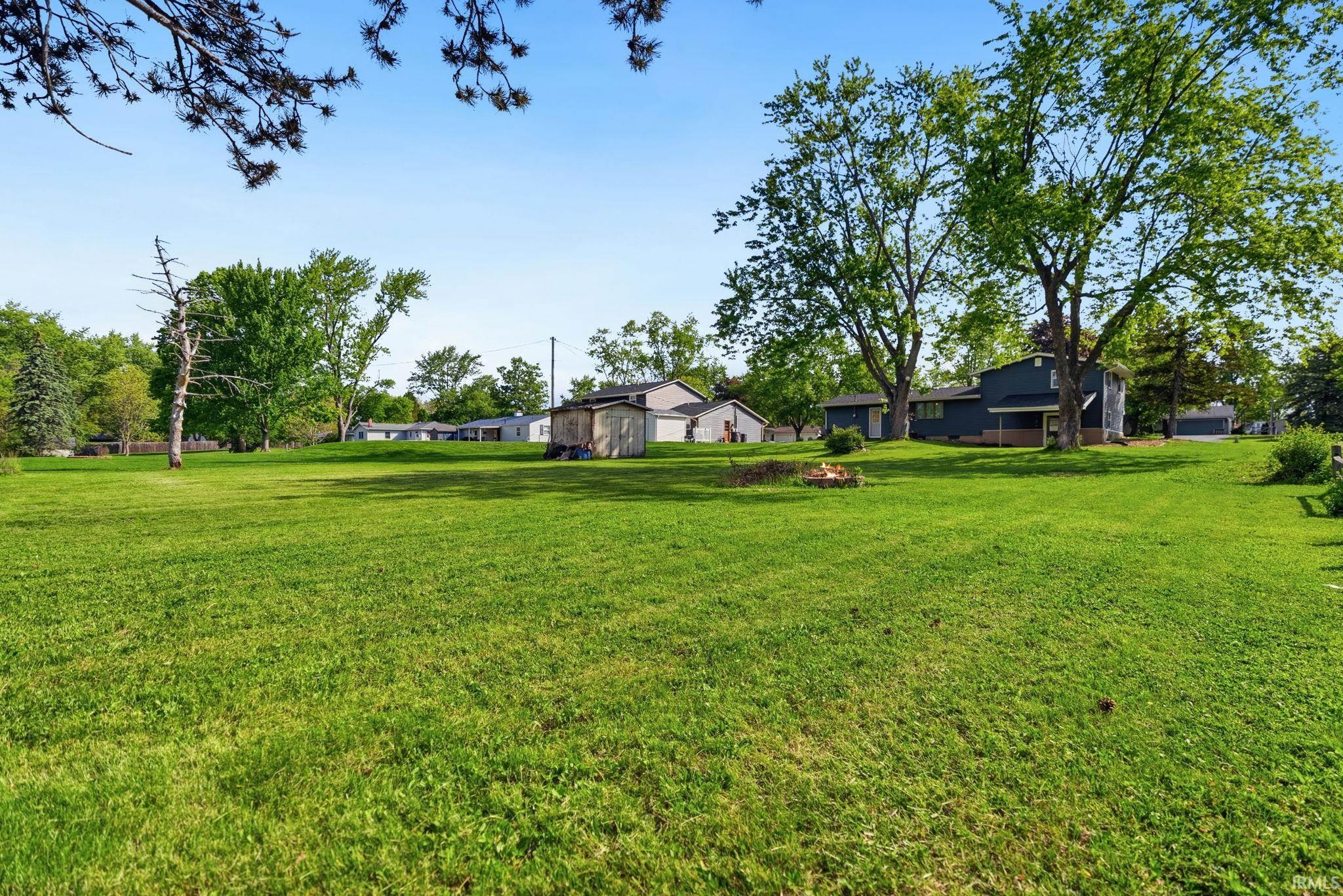 Expansive green lawn with mature trees and a visible residential structure in the background