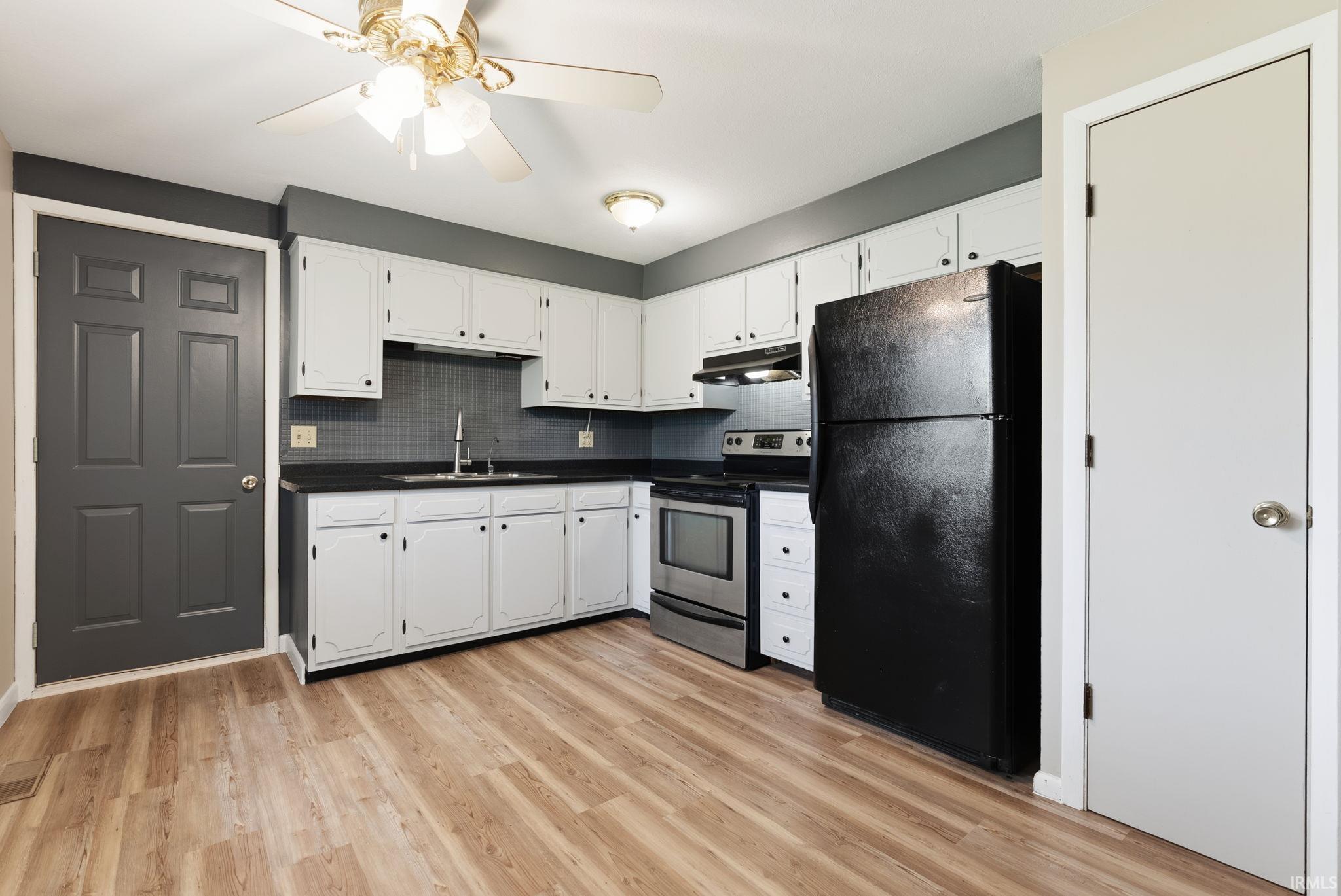 Kitchen featuring wood-finish flooring, white cabinetry, dark countertops, a tiled backsplash, and a ceiling fan with integrated lighting