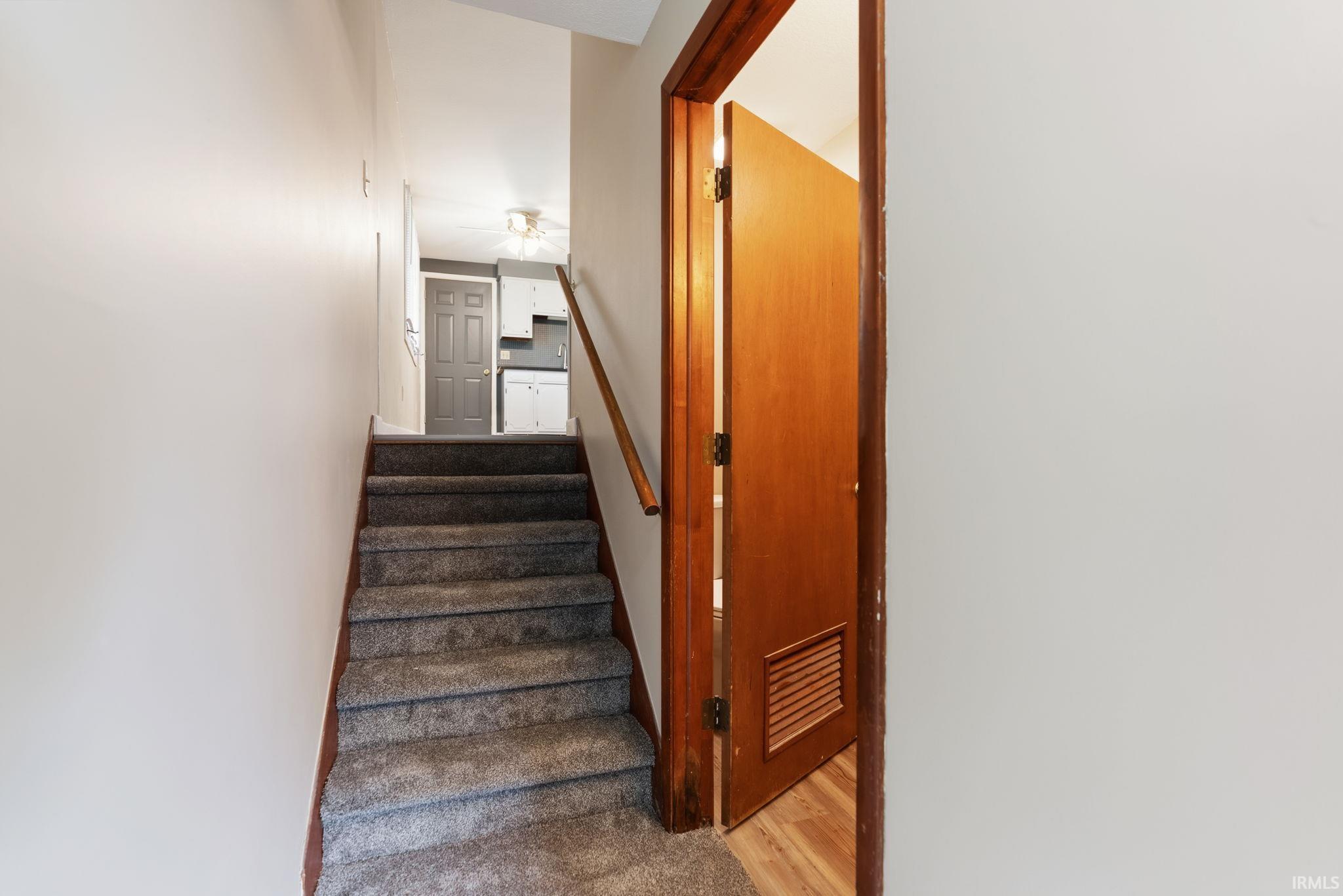 Carpeted staircase with wooden handrail, leading to an upper level with a visible kitchen area