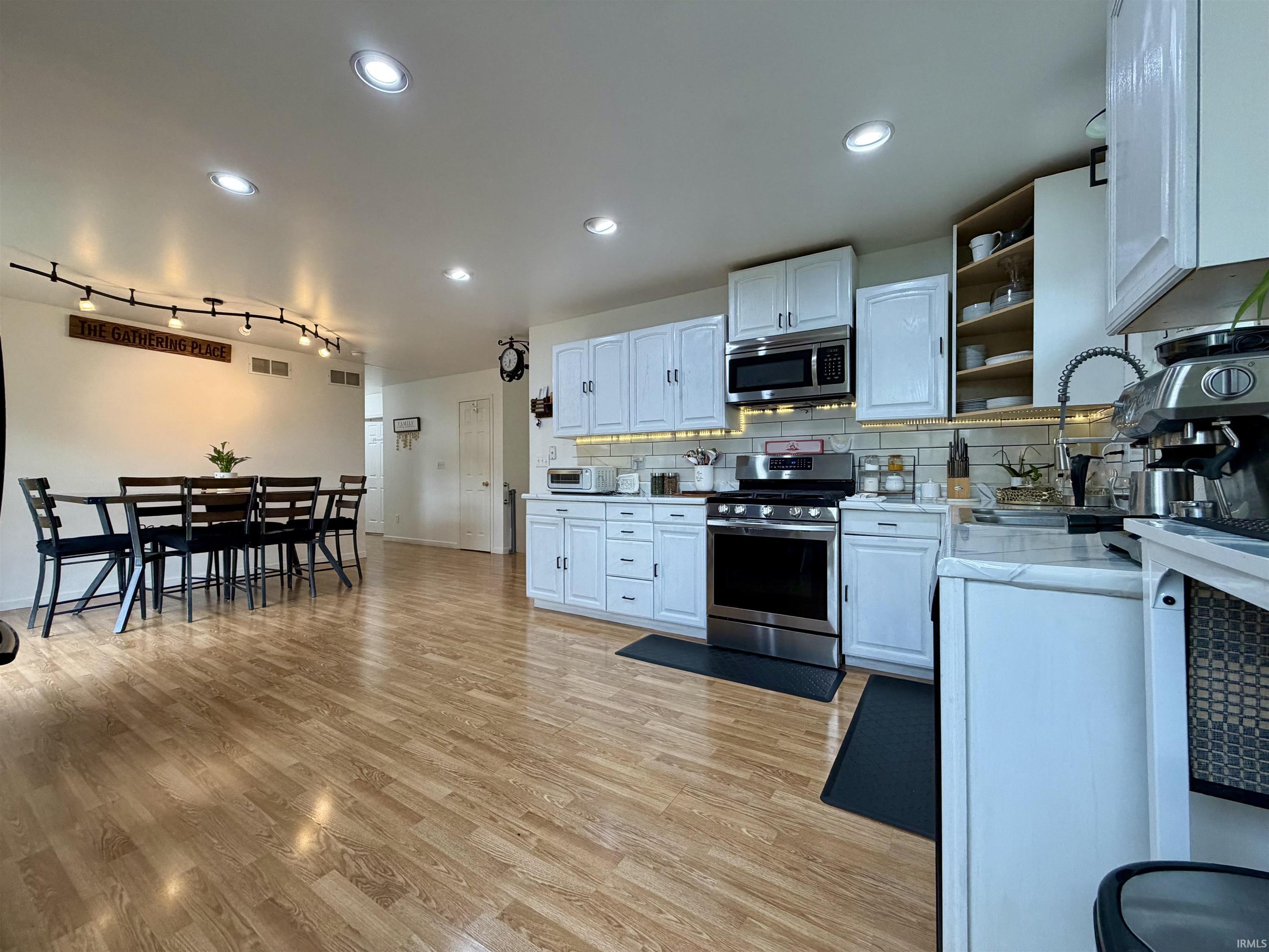 Open-concept kitchen and dining area featuring light wood-finish flooring, white cabinetry, stainless steel appliances, and recessed lighting