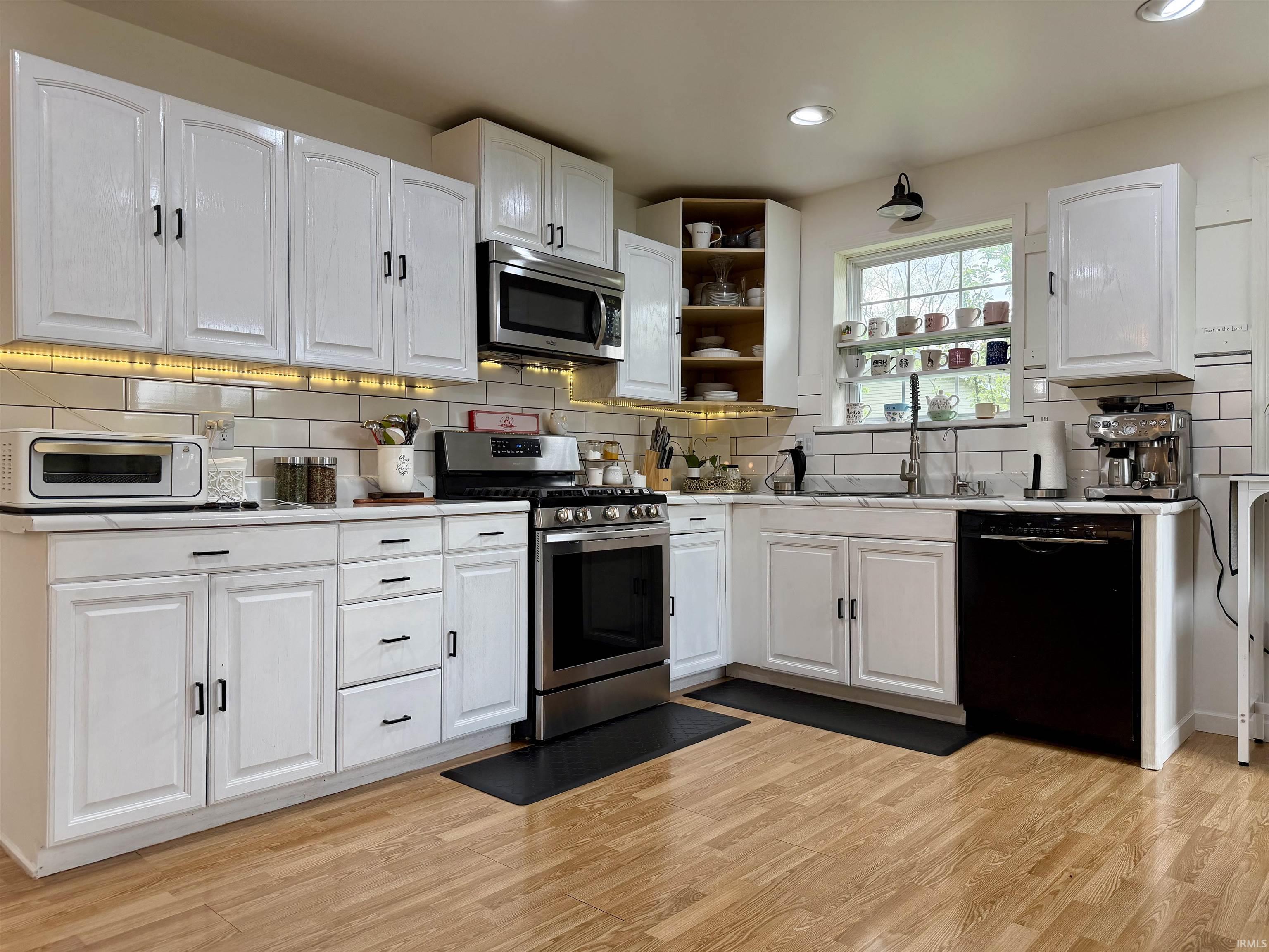 Kitchen featuring white cabinetry, light countertops, wood-finish flooring, subway tile backsplash, and stainless steel appliances