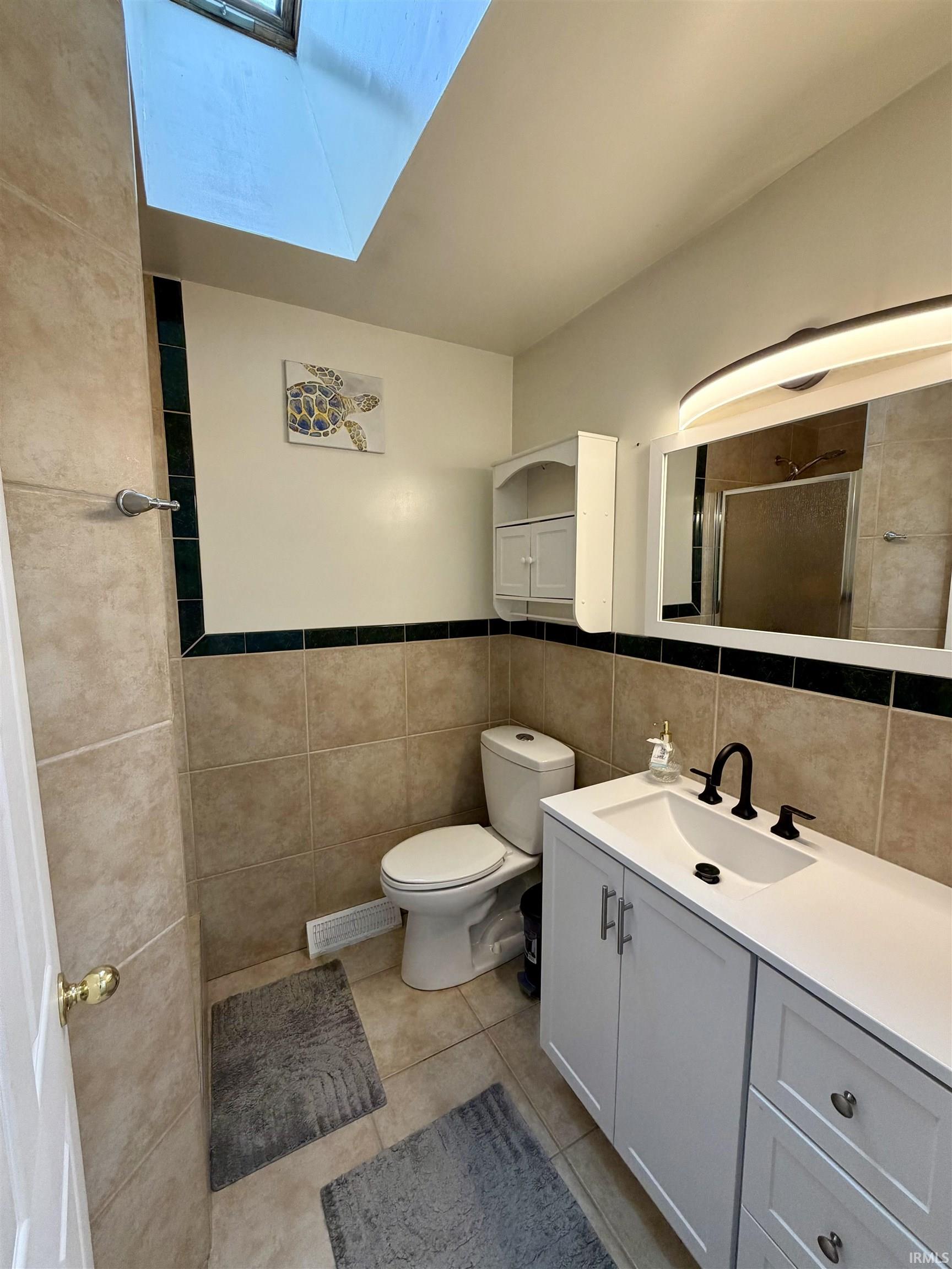 Bathroom featuring a white vanity with integrated sink, a large mirror with integrated lighting, and a skylight