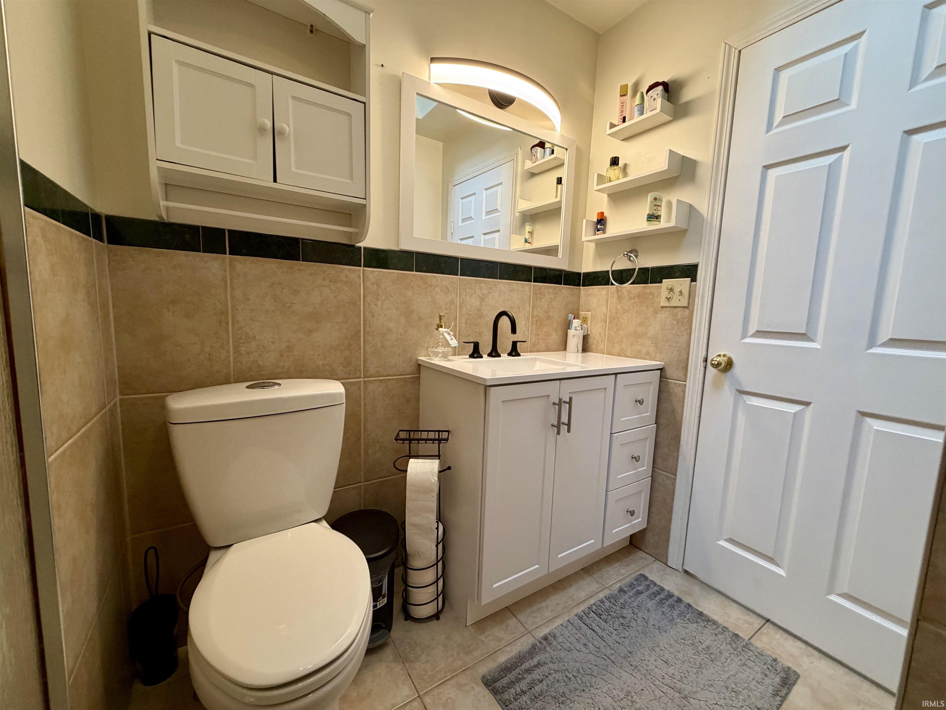 Bathroom featuring a white vanity with a dark faucet, a wall-mounted medicine cabinet, and tiled walls