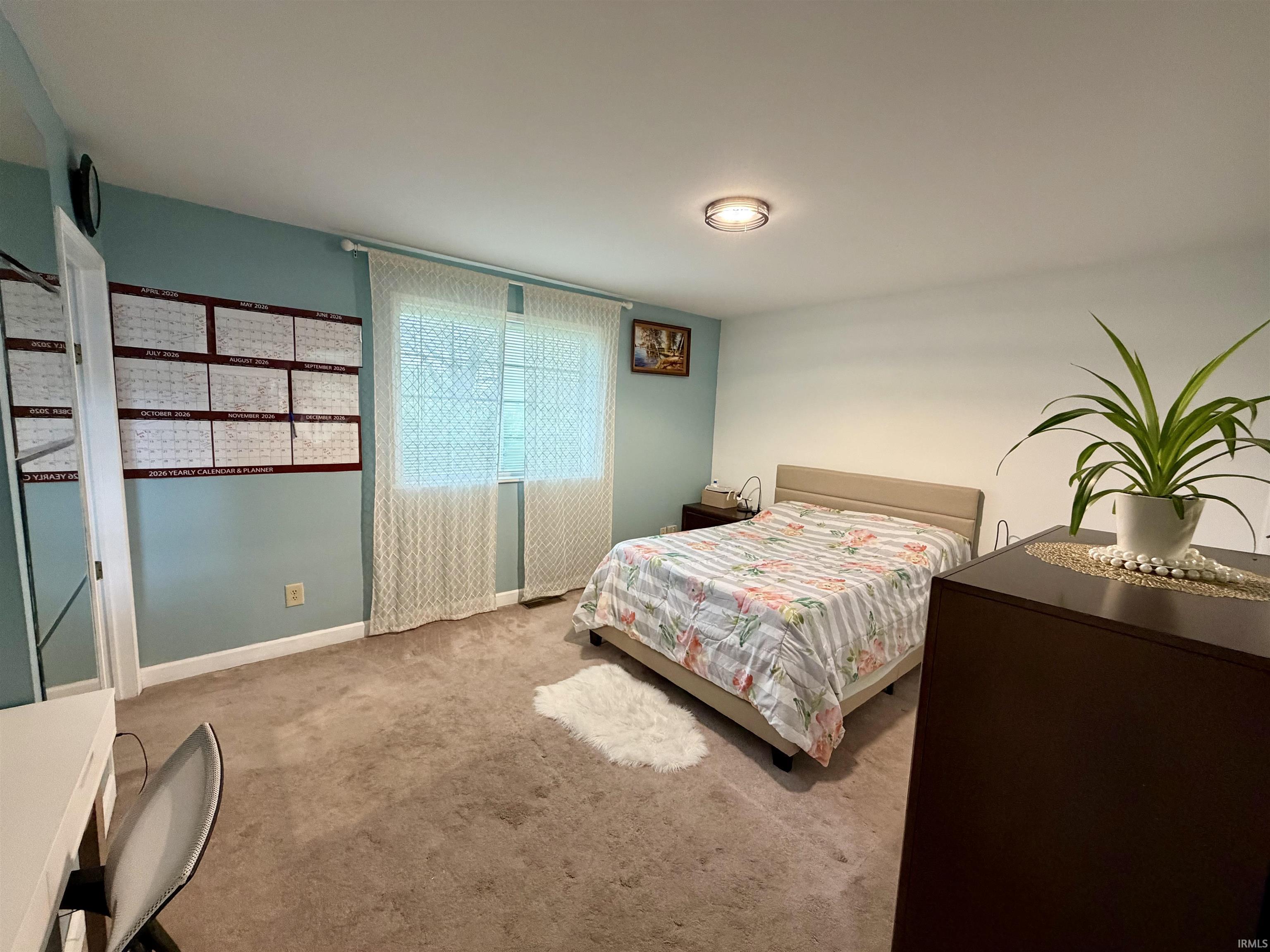 Carpeted bedroom featuring a window with sheer curtains, a light blue accent wall, and a ceiling-mounted light fixture