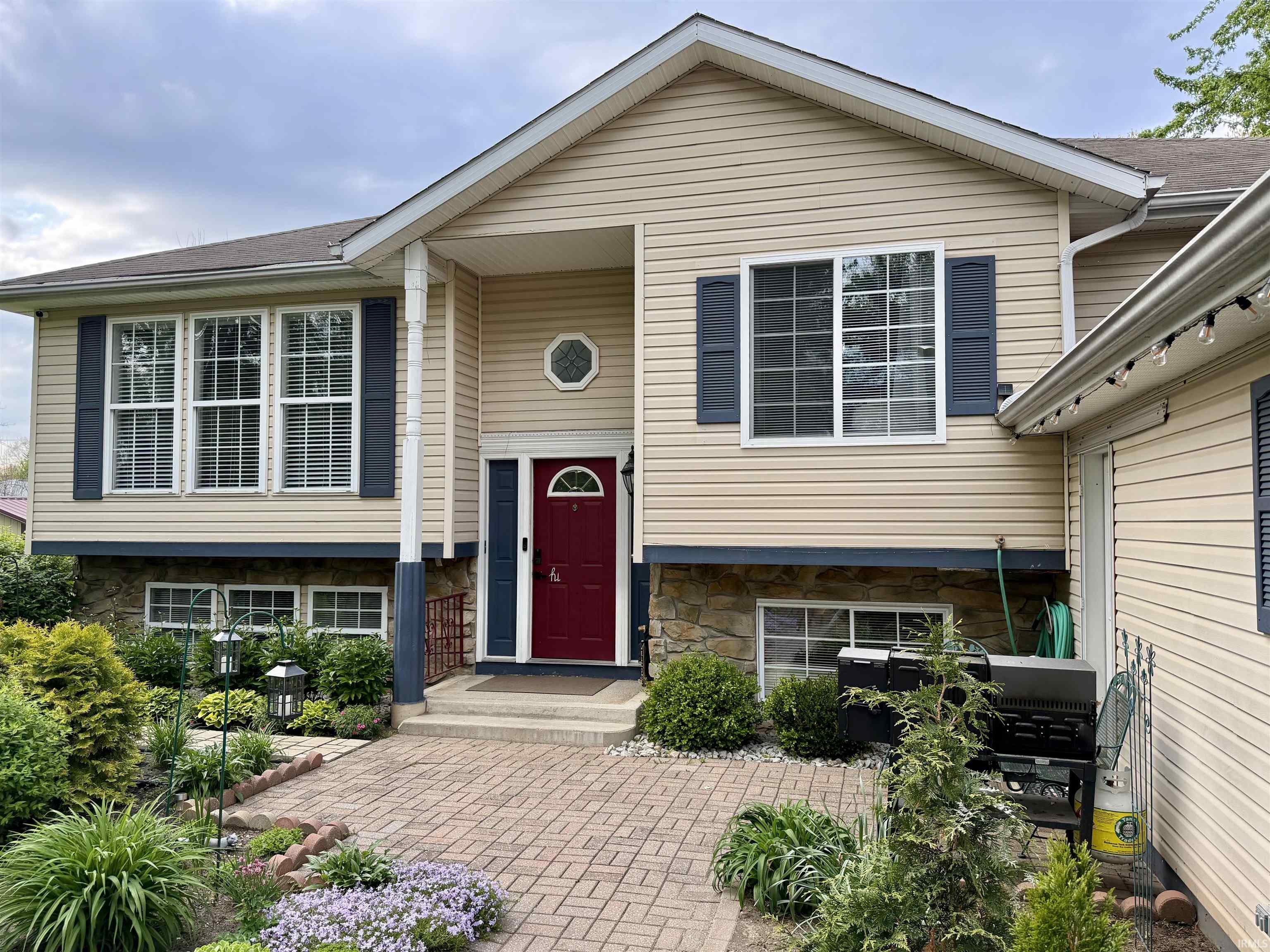 Split-level exterior featuring tan siding, dark blue shutters, a prominent red front door, and a stone facade