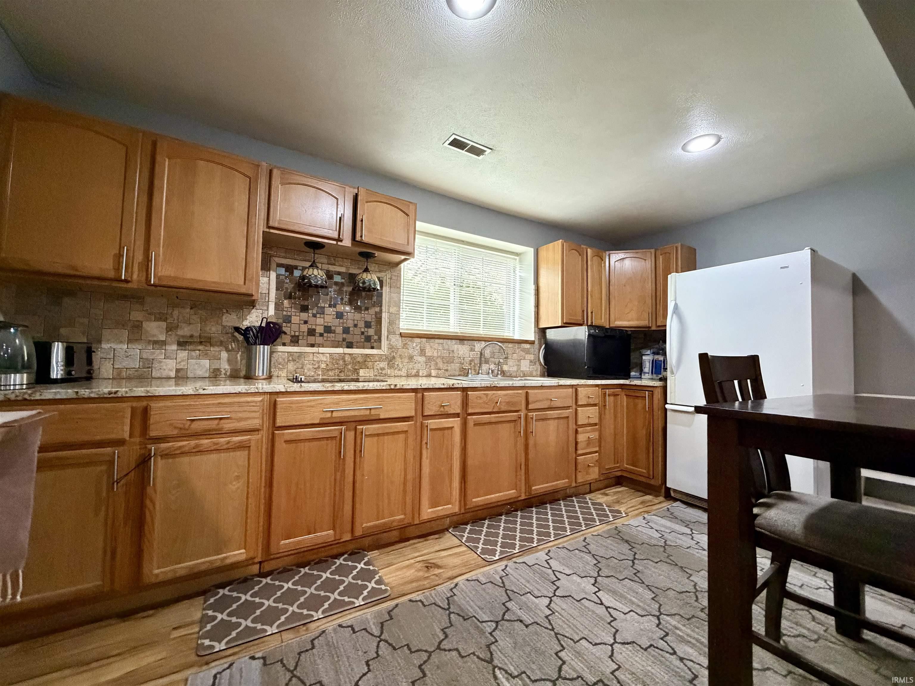 Kitchen featuring light wood cabinetry, granite countertops, a mosaic tile backsplash, and wood-finish flooring