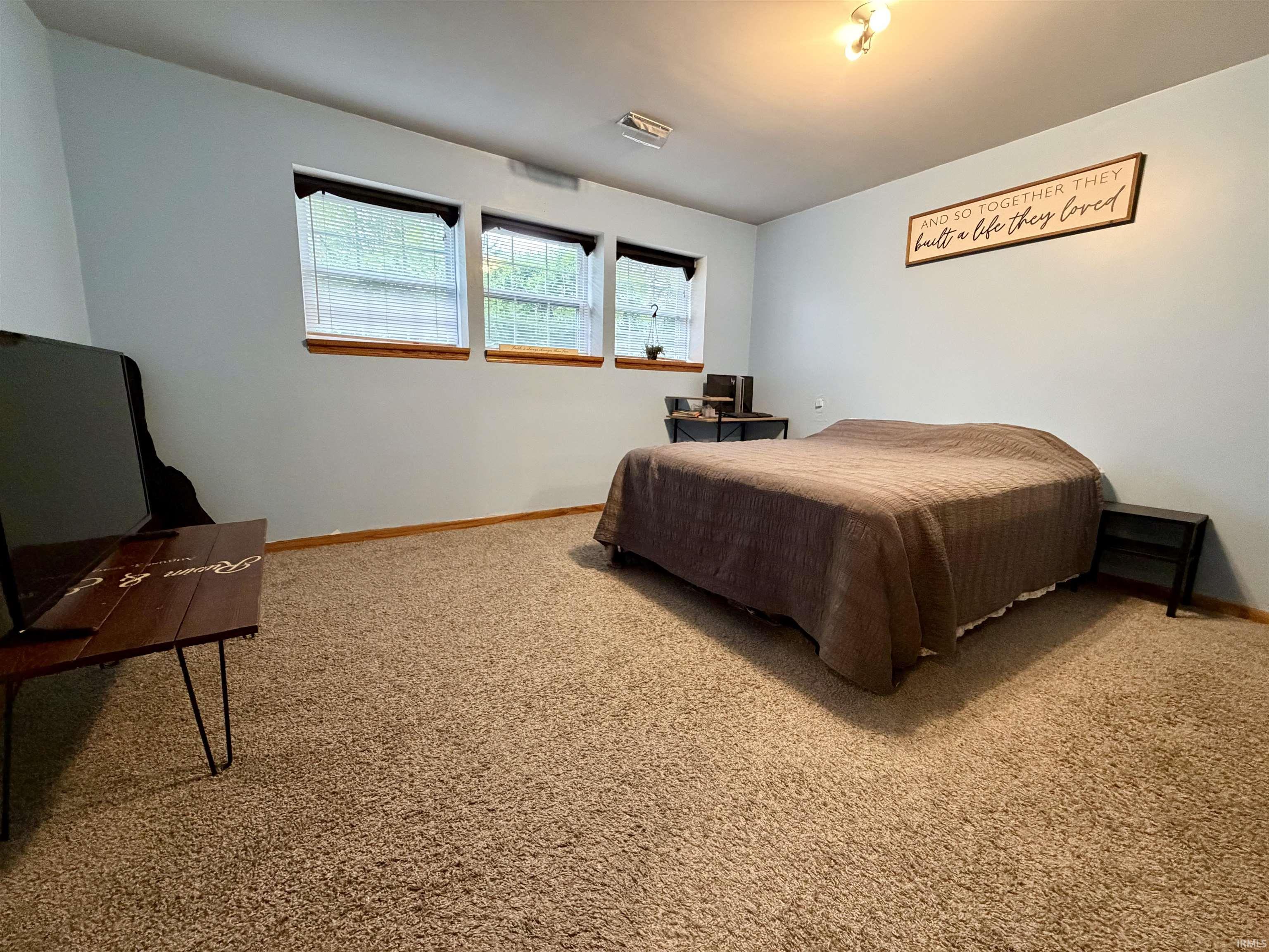Spacious room featuring light blue walls, plush carpeting, three windows with wood trim, and a ceiling-mounted light fixture