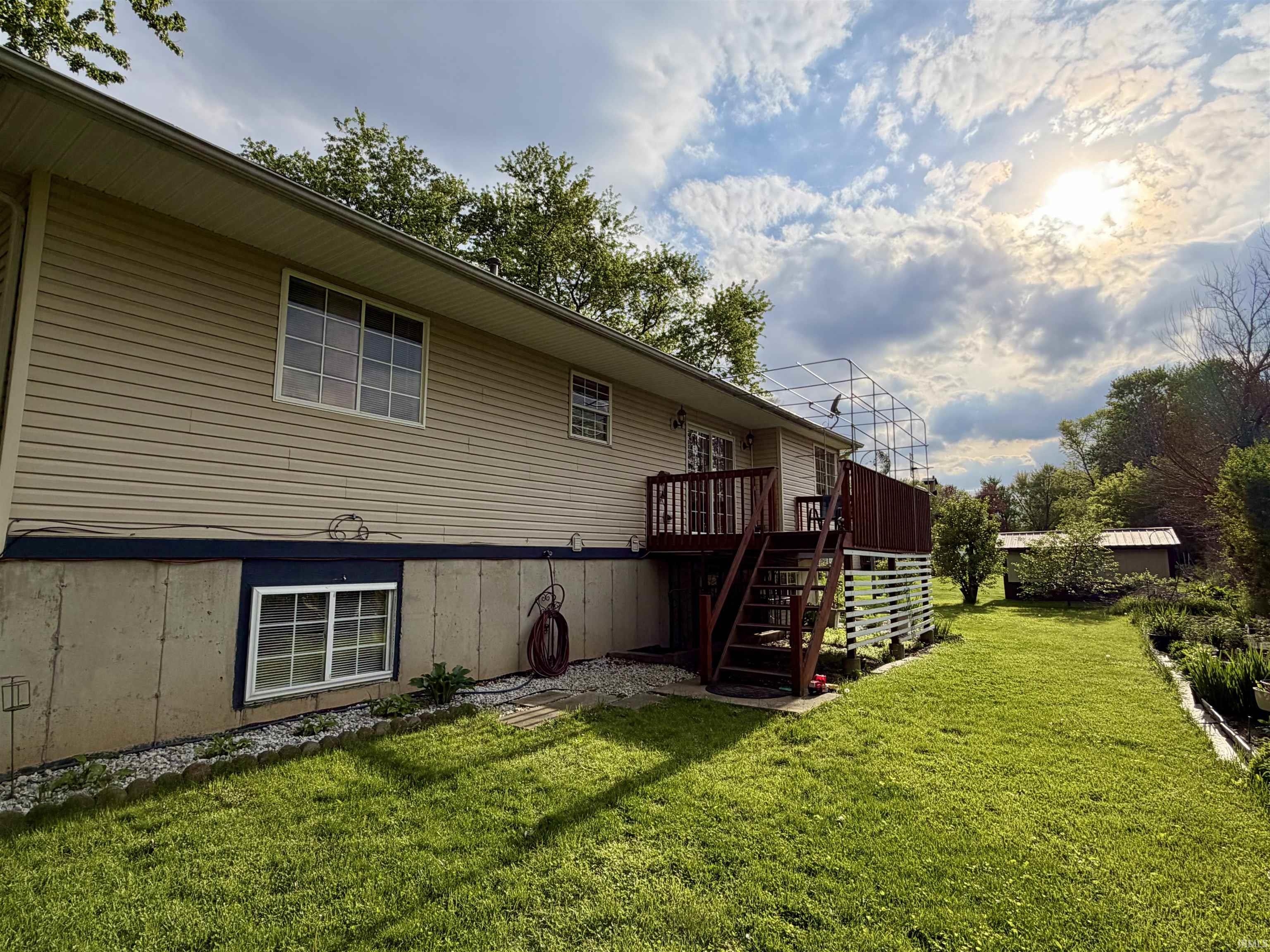 Expansive green lawn with a two-story home featuring tan siding and a dark stained wood deck