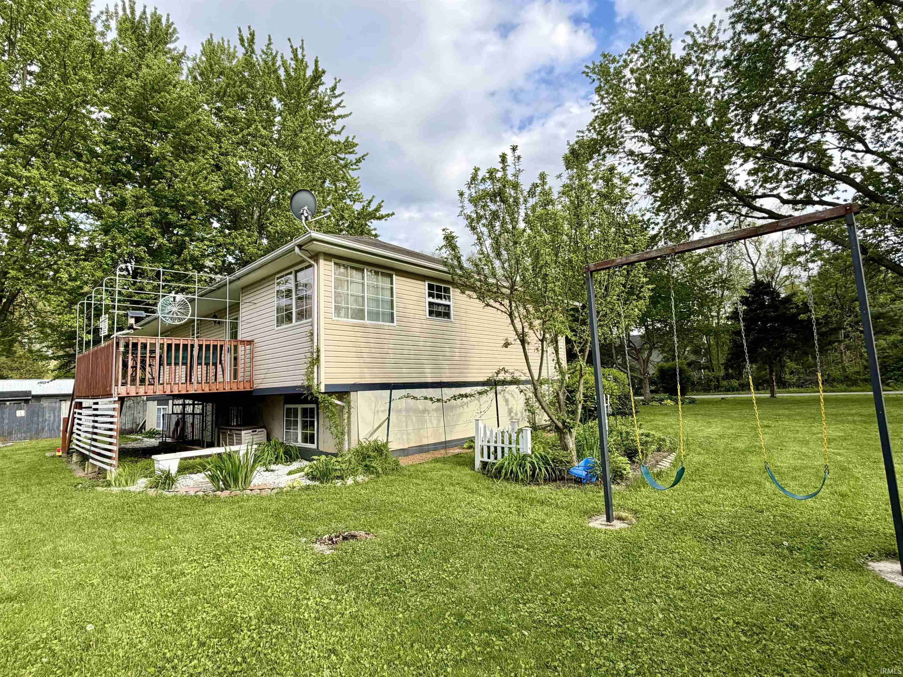 Split-level residence featuring a raised wood deck, light-toned siding, and multiple windows