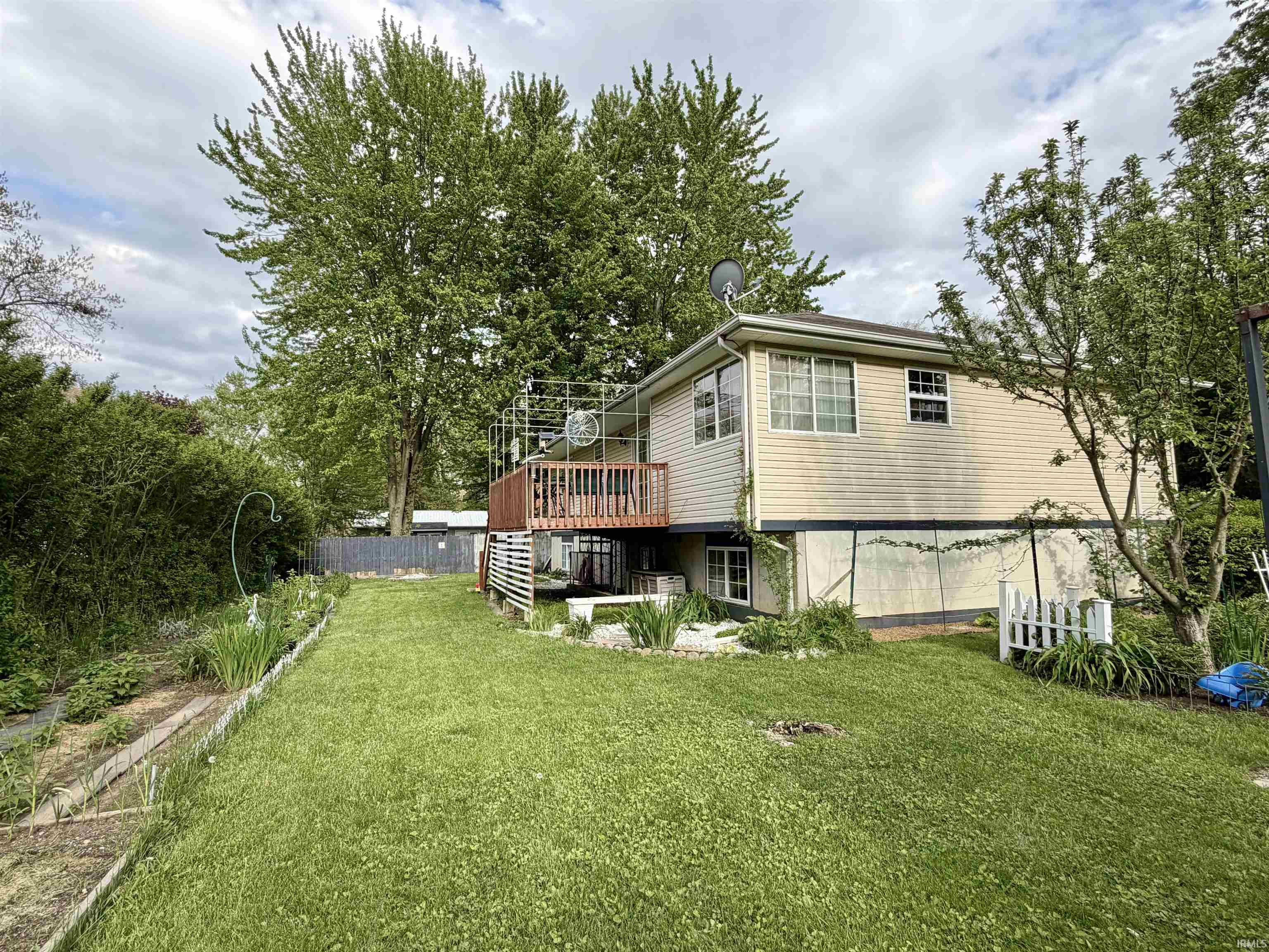 Expansive backyard featuring a green lawn, established garden beds, mature trees, and a privacy fence