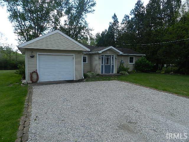Front exterior featuring a gravel driveway, attached garage, and light-colored siding