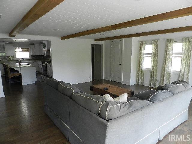 Open-concept living area with dark wood-finish flooring, white walls, and a white plank ceiling with exposed wood beams