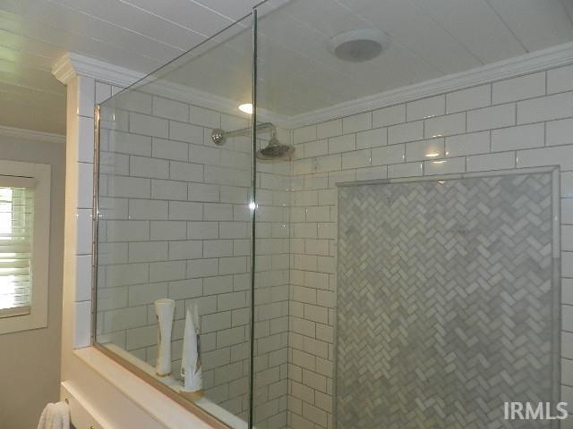 Glass-enclosed shower featuring white subway tile, a recessed niche with herringbone tile, a chrome rain shower head, and crown molding