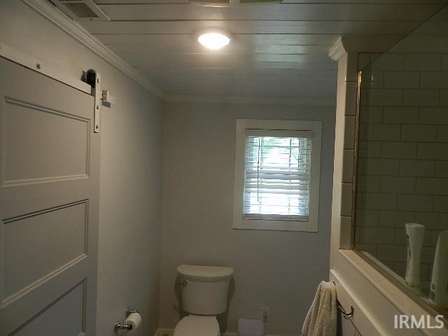 Bathroom featuring a white paneled barn door, a window with horizontal blinds, a white toilet, subway tile shower surround, and a planked ceiling