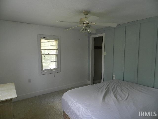 Bedroom featuring a window with blinds, ceiling fan, carpet flooring, and a blue accent wall with vertical paneling