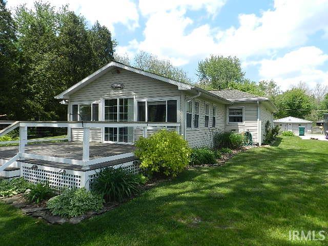 Exterior siding residence featuring a large wood-finish deck with white railings and lattice skirting, mature landscaping, expansive lawn, and a detached garage structure