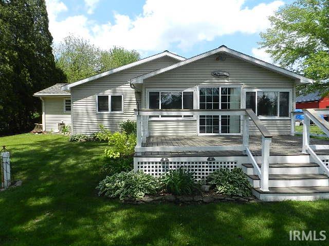 Exterior siding home featuring a multi-level deck with white railings and steps, multiple windows, and a well-maintained lawn with mature landscaping