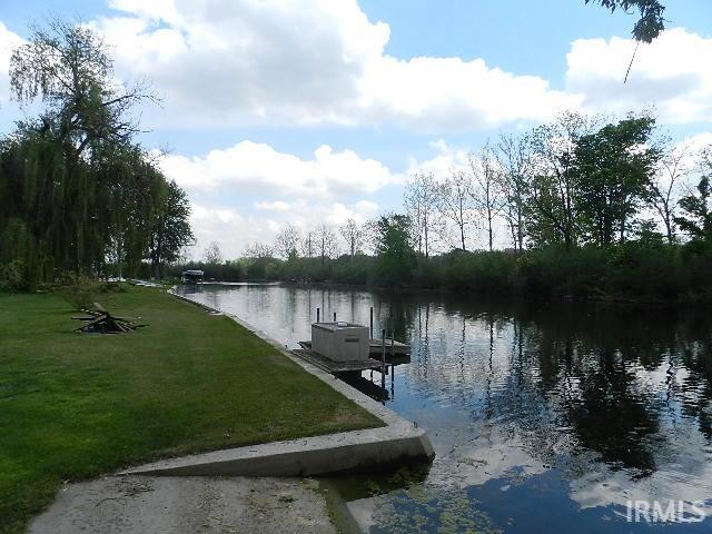 Waterfront property featuring a concrete seawall, expansive grassy area, and mature trees