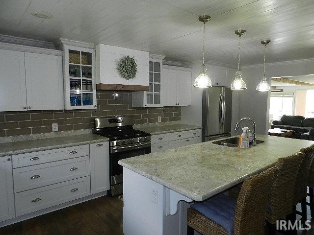 Kitchen featuring white cabinetry, subway tile backsplash, stainless steel appliances, and a central island with an undermount sink