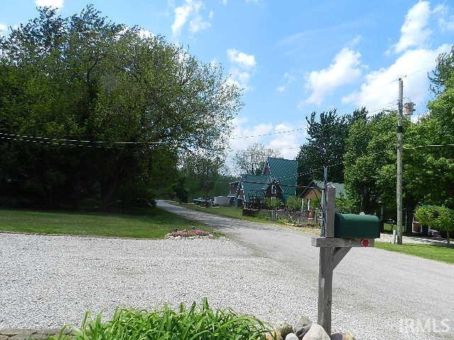 Gravel driveway leading to residences with green metal roofs and mature trees