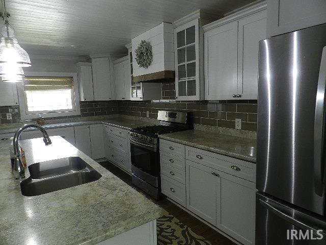 Kitchen featuring white shaker-style cabinetry, a gray subway tile backsplash, light-toned countertops, stainless steel appliances, and a built-in range hood with shiplap detailing