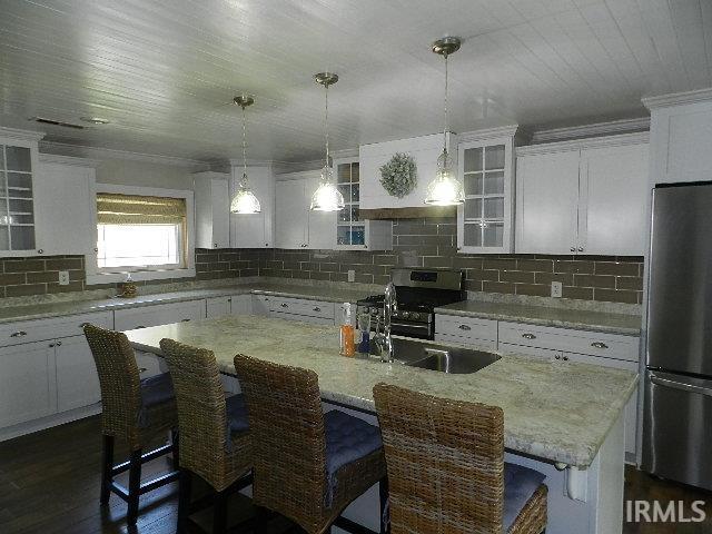 Kitchen featuring an expansive island with an undermount sink, white cabinetry, subway tile backsplash, stainless steel appliances, and a plank ceiling